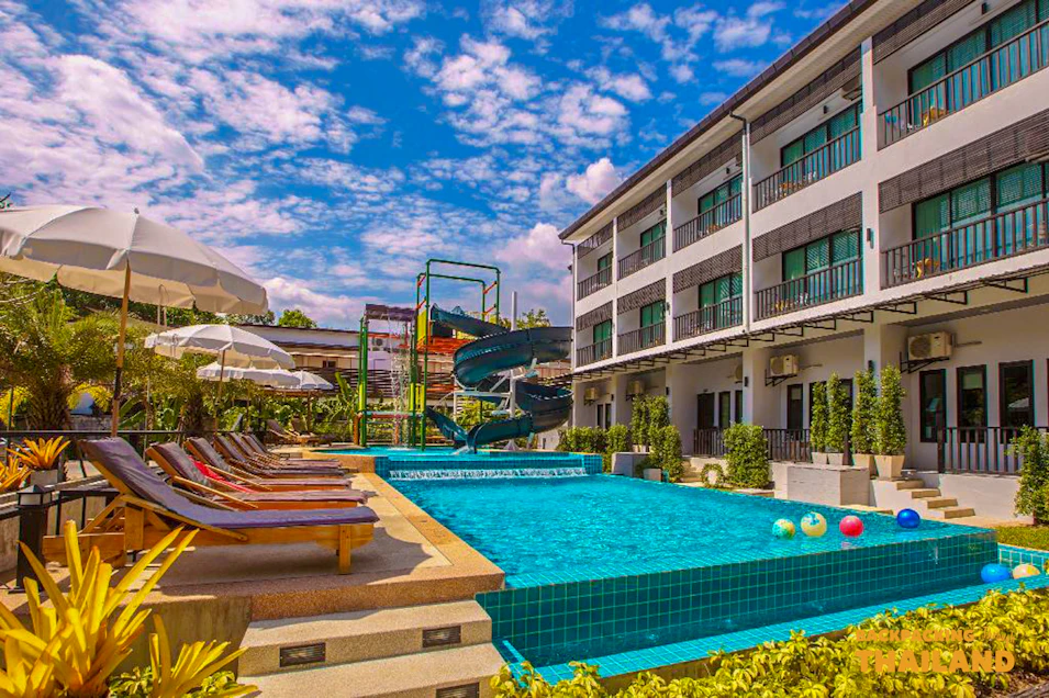 A vibrant resort pool with a water slide and sun loungers under a blue sky in Thailand.