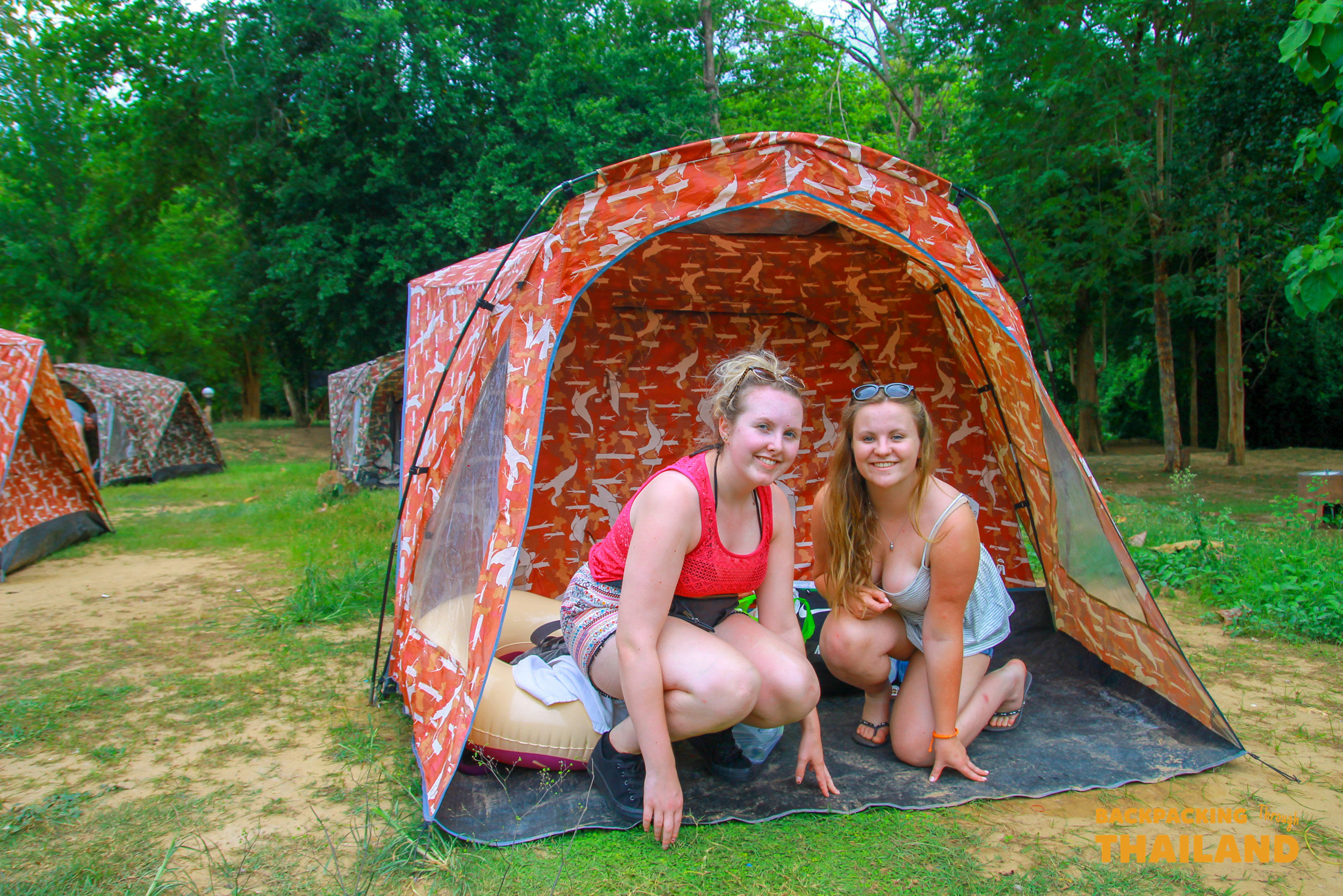 Two travellers sitting together in front of a camouflage-pattern tent at the campsite