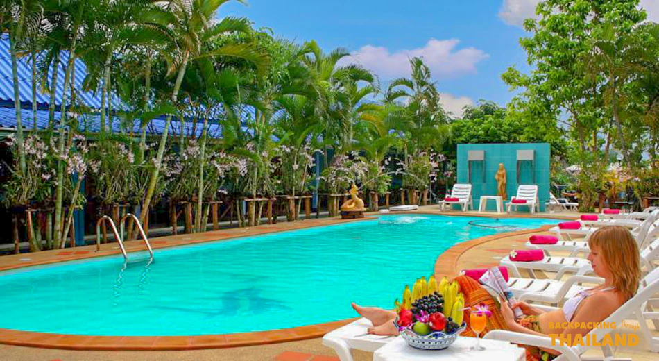 A woman relaxes by a vibrant blue swimming pool at a tropical resort in Thailand.