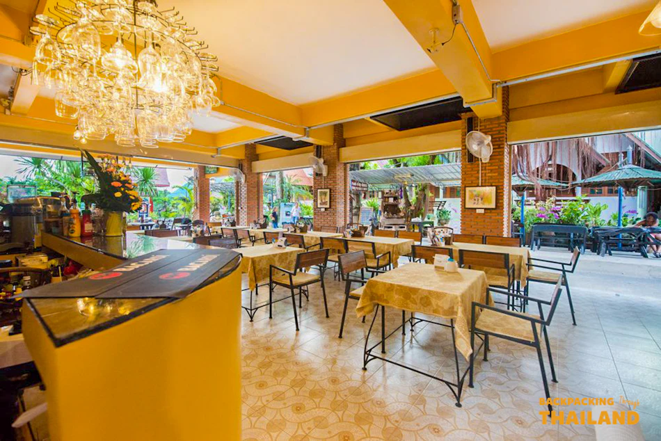 A bright, open-air restaurant with yellow walls, many tables, and a large chandelier in Kanchanaburi.