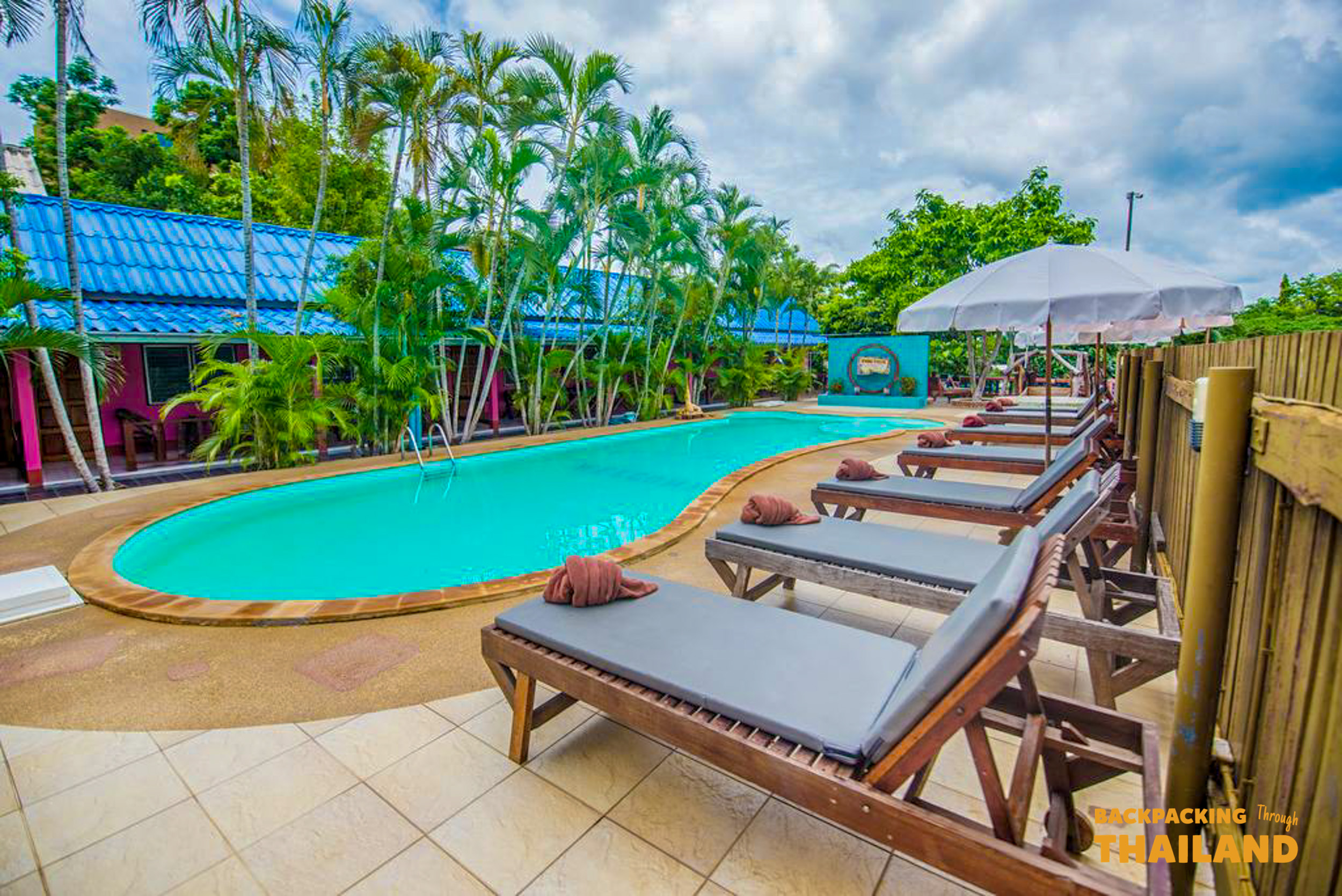 Vibrant resort buildings surrounding a swimming pool with turquoise water and palm trees