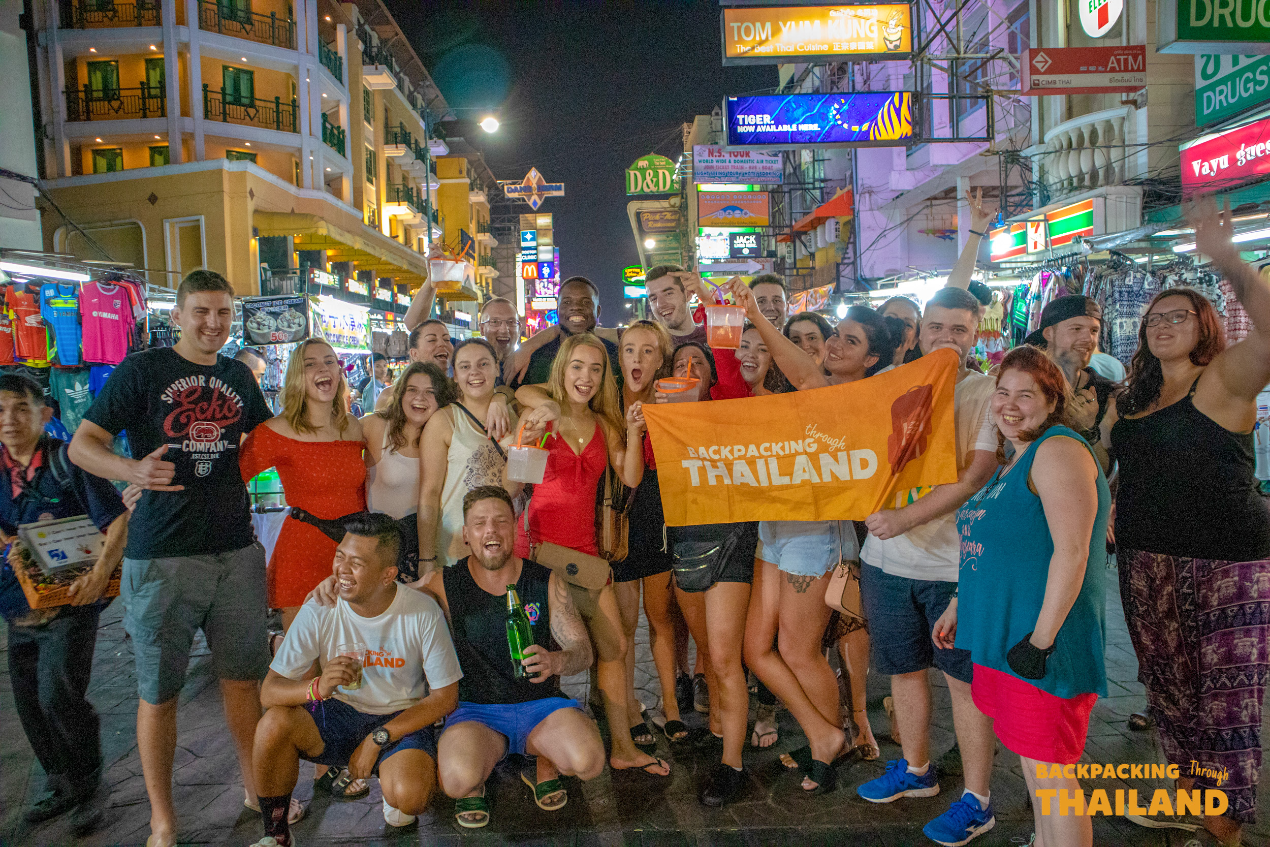 Backpacking Tour group holding the 'Backpacking Thailand' flag on Khao San Road, Bangkok.