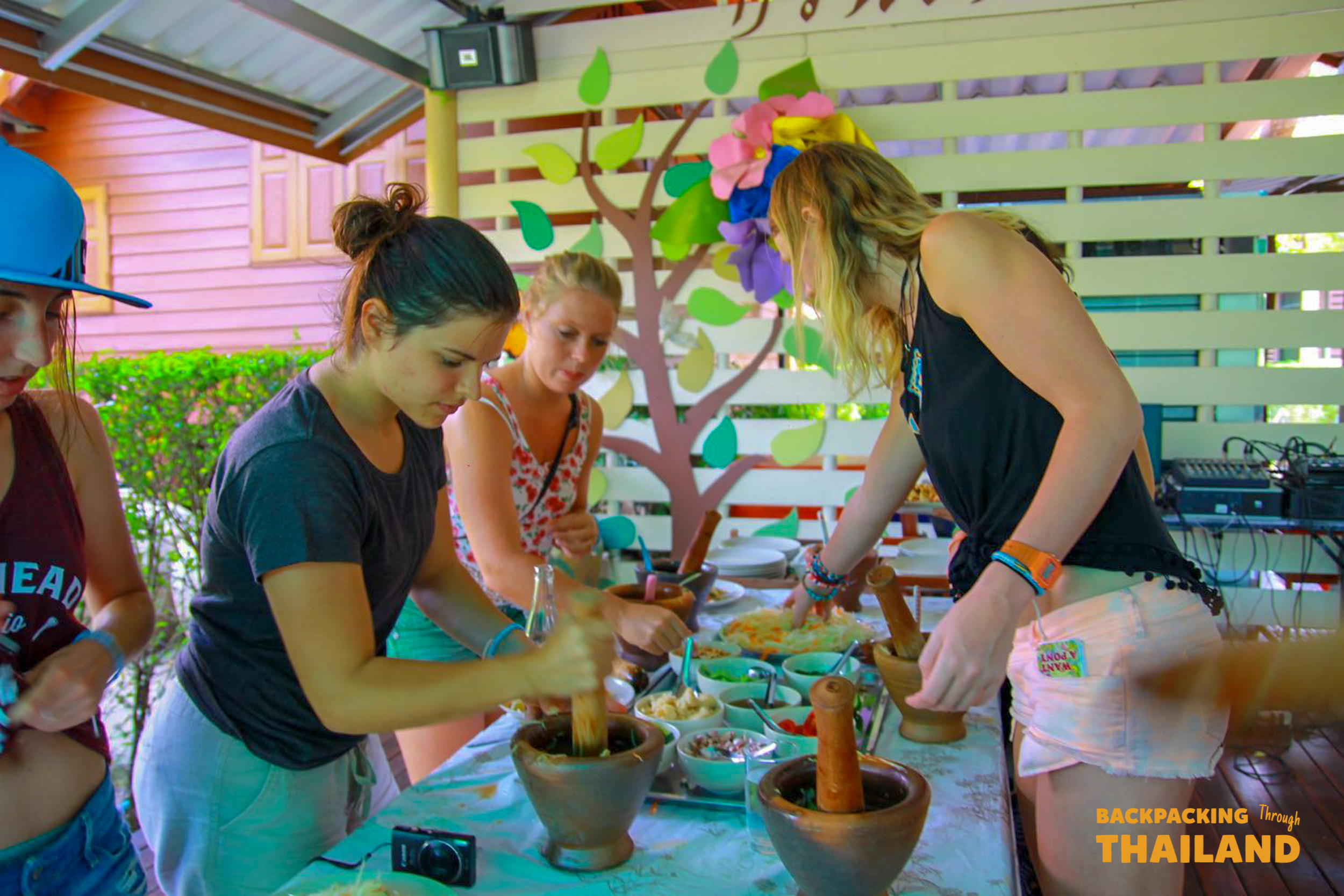 Backpacking travellers preparing Thai food together at a homestay cooking lessonBackpacking travellers cooking together with a local host at a homestay, using a large wok