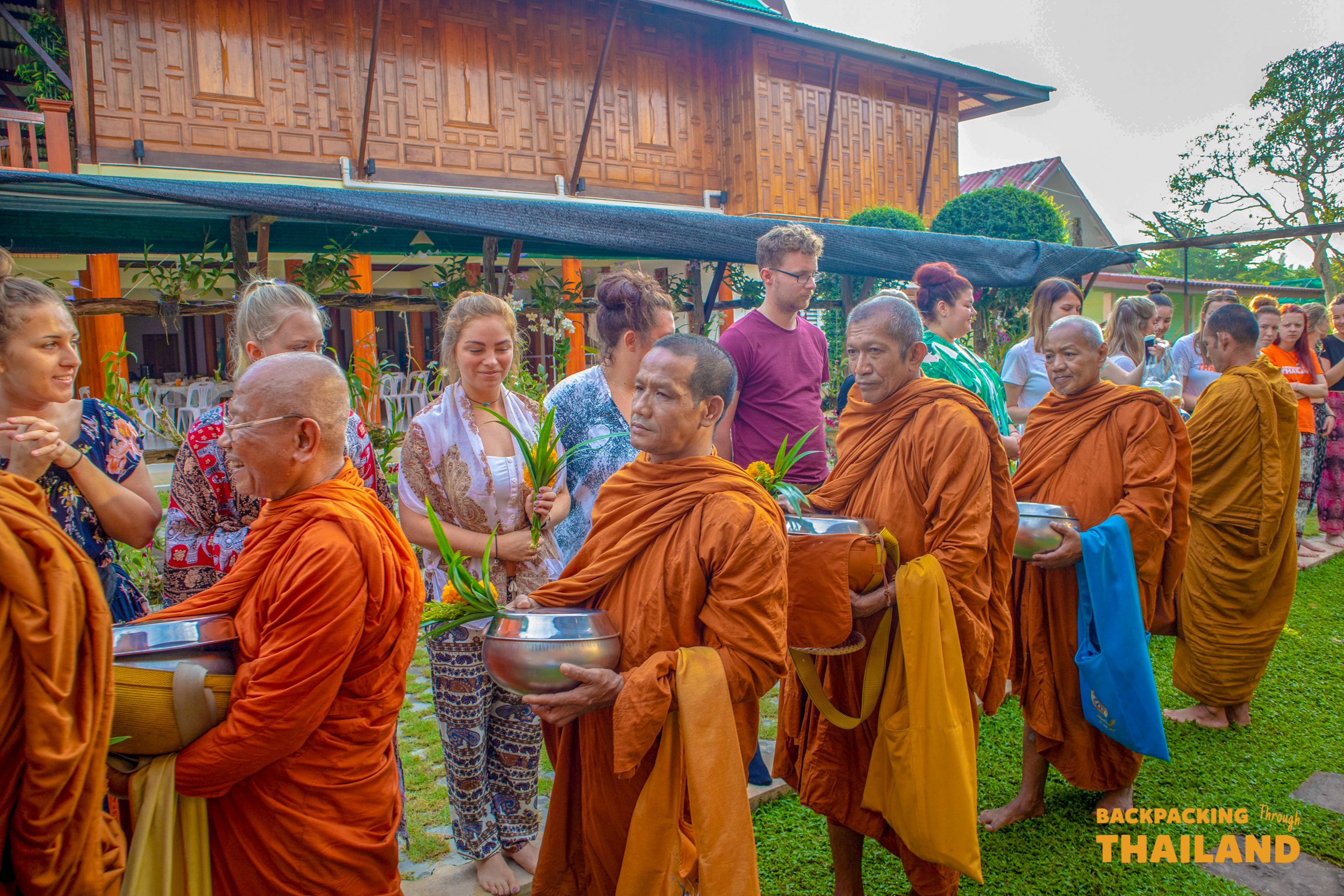 Line of orange-robed monks receiving alms from people during a morning merit ceremony