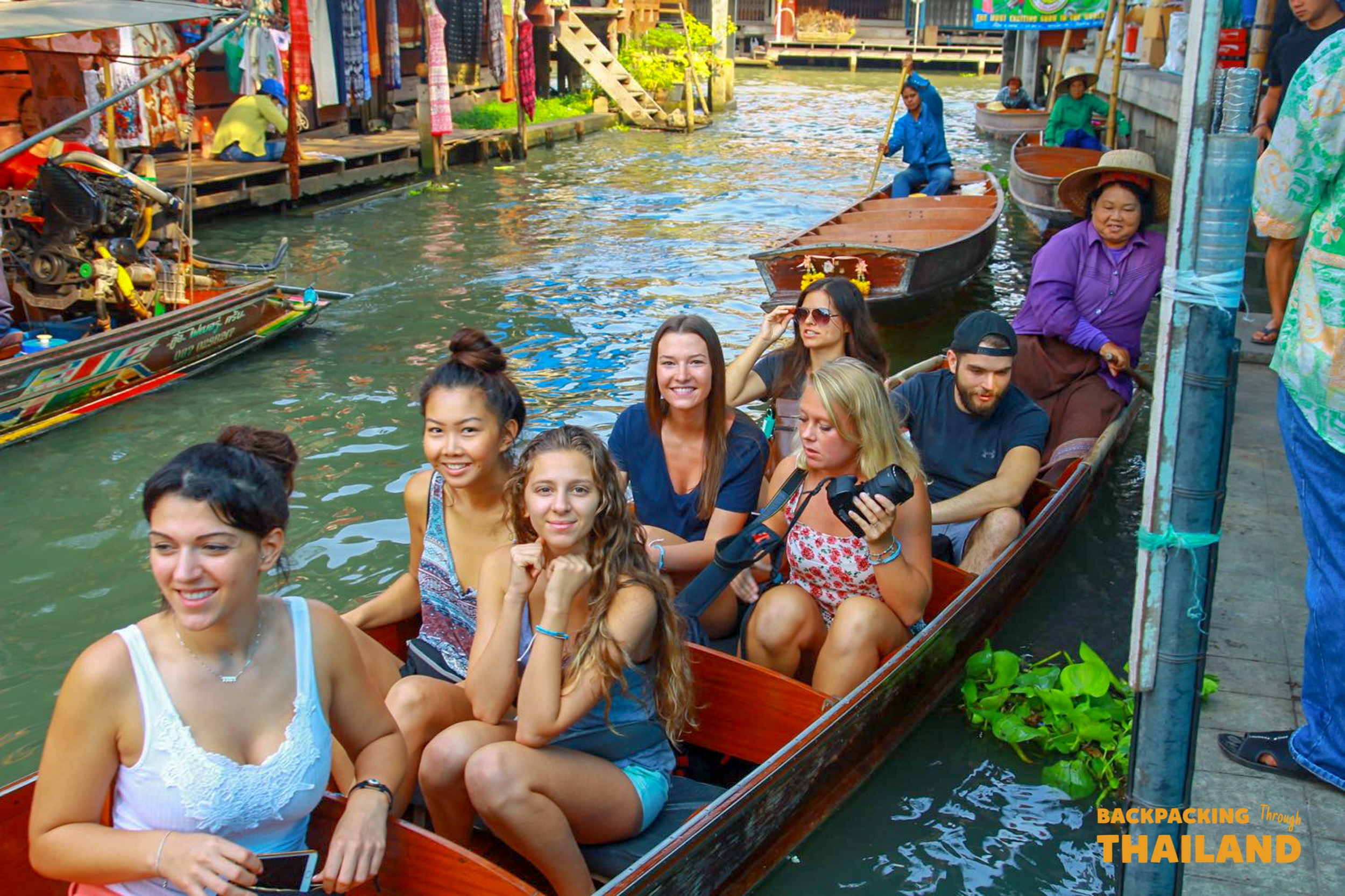 Backpacking group sitting in a wooden boat while a local guide paddles through a floating market canal