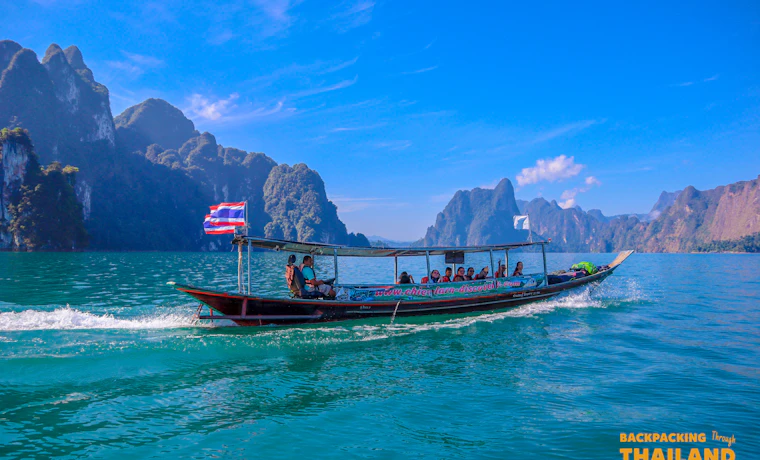 Longtail boat cruising across Khao Sok lake with Thai flag.