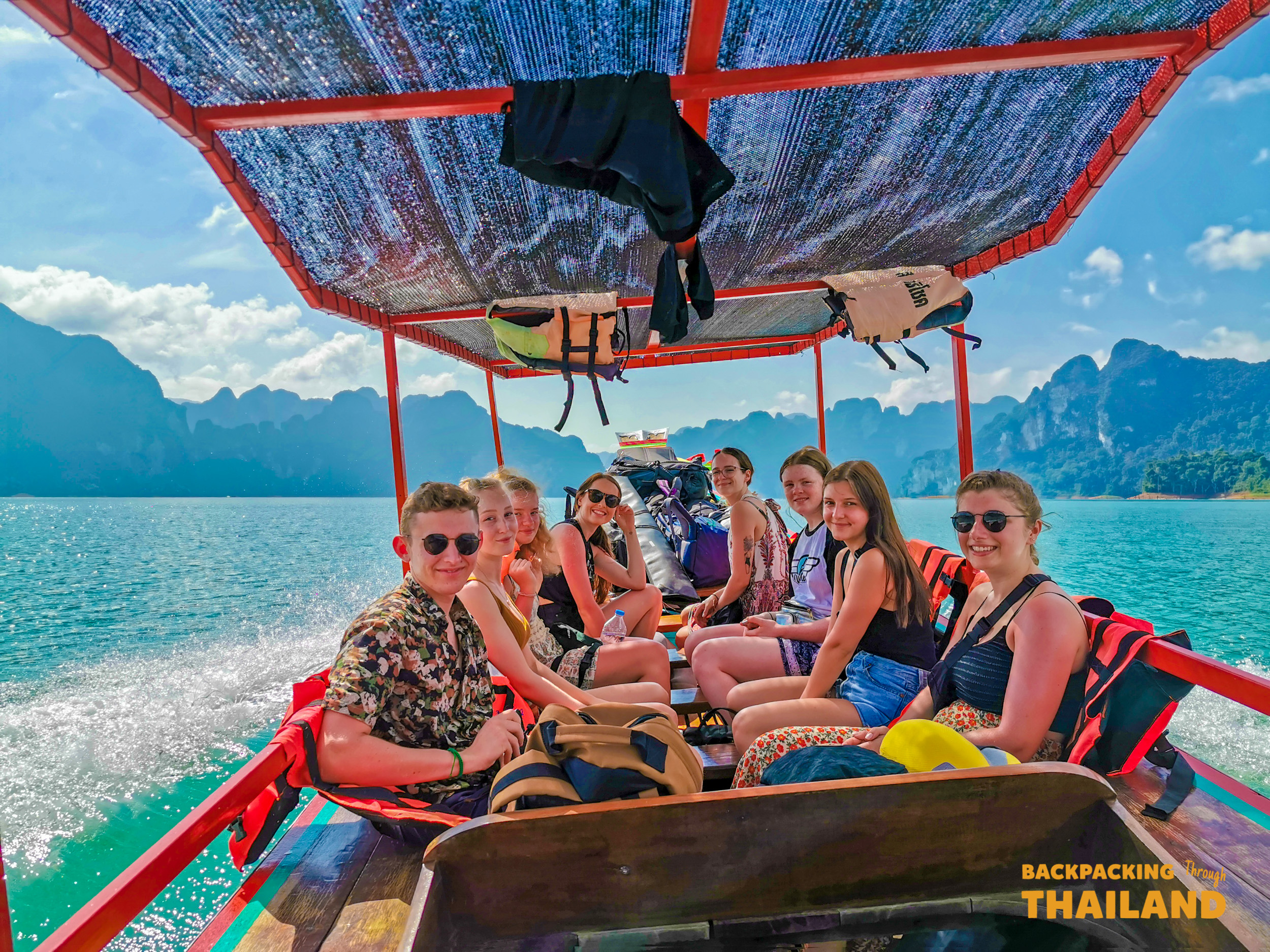 Travellers enjoy a group boat tour on a turquoise lake with a colourful canopy, Day 8 activityLongtail boat cruising through emerald waters against towering limestone cliffs, Day 8 activity