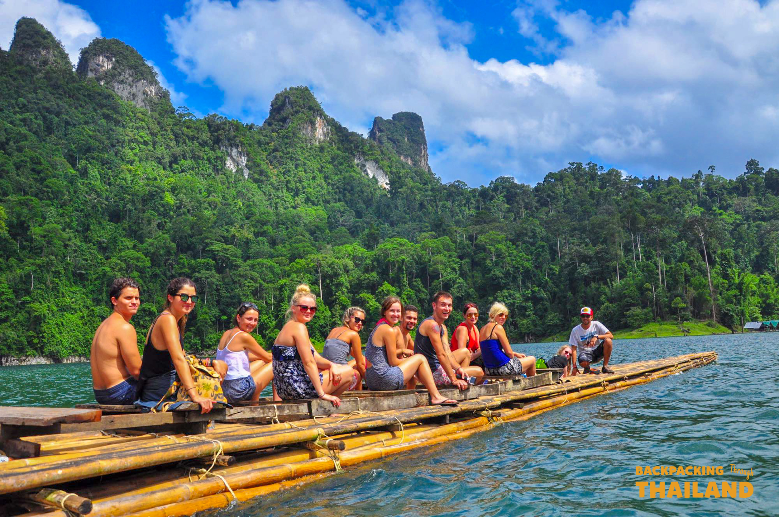 Group of travellers sitting on a bamboo raft on a turquoise lake with mountains in the background, Day 8 activity