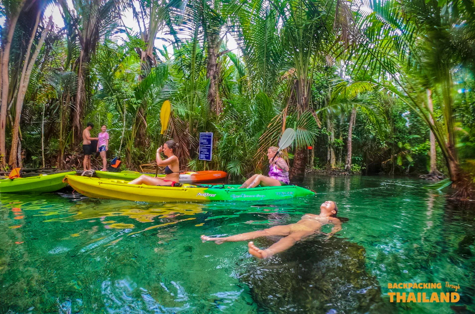 Adventurous travelers kayaking and relaxing in a beautiful clear turquoise jungle pool in Thailand.