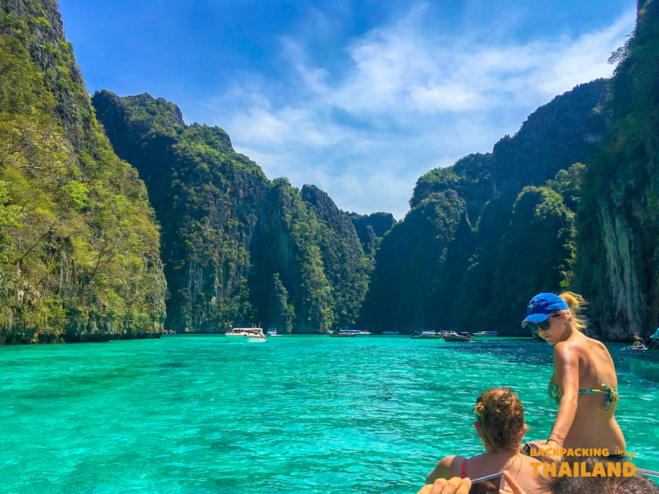 Travelers on a boat in Thailand's Phi Phi Islands, admiring the turquoise water and towering limestone cliffs.