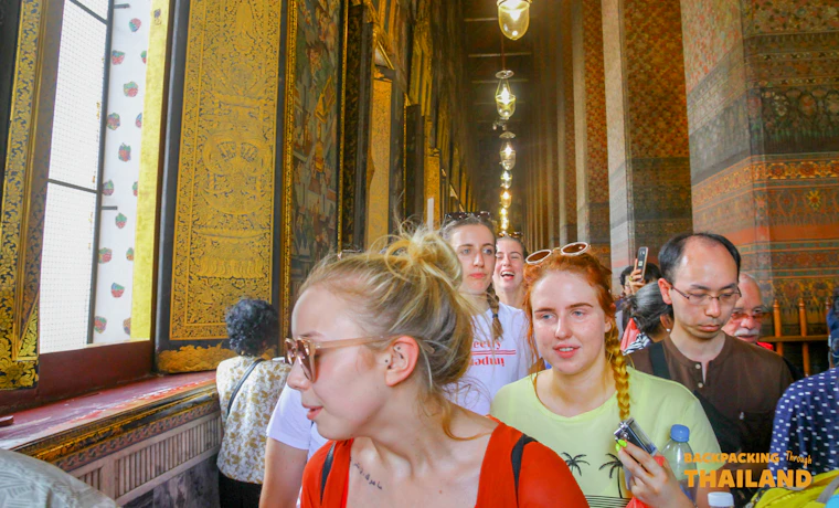 A group of backpackers walks through a stunning golden temple corridor, admiring the intricate details in Bangkok.