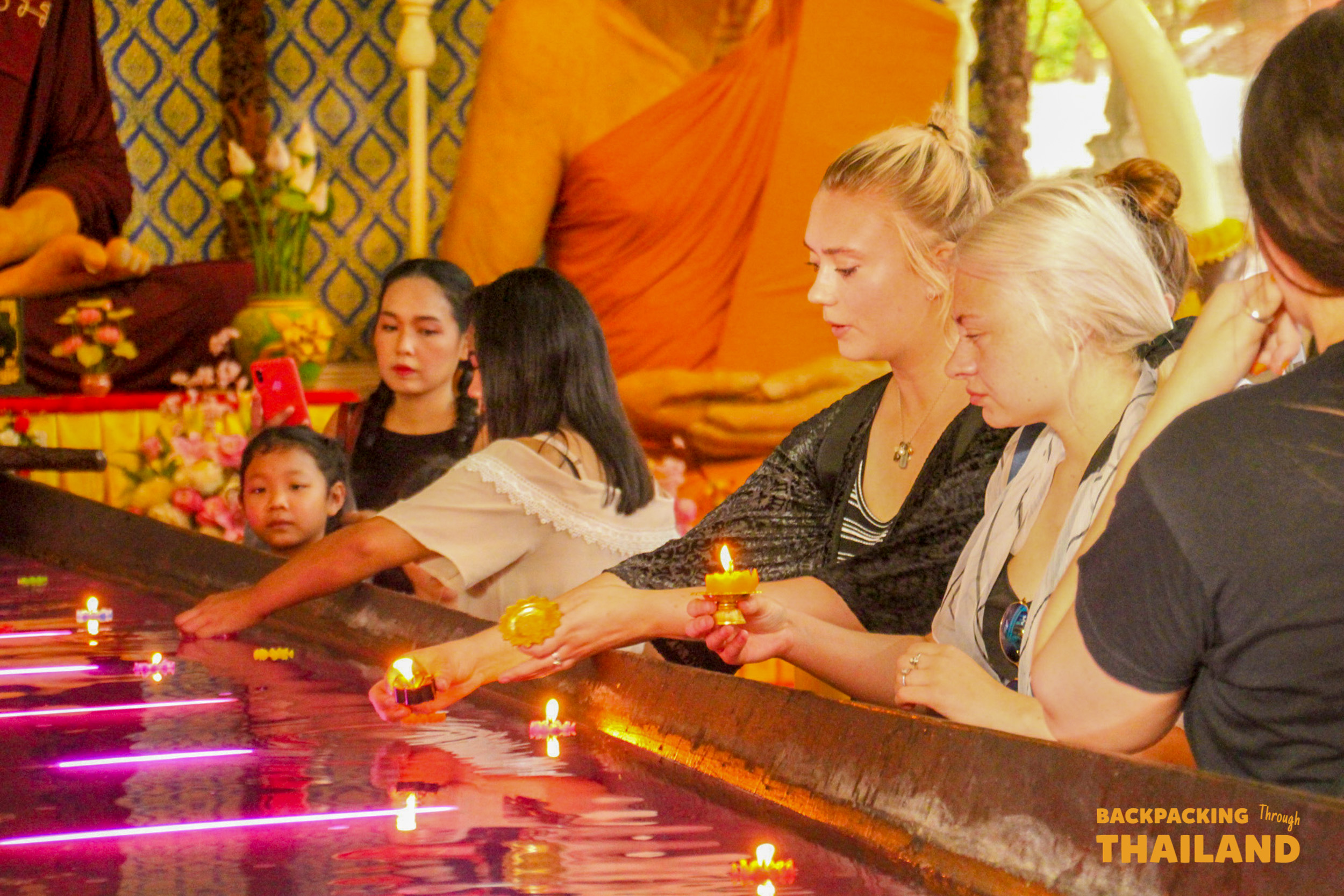 Travelers respectfully float candles in a purple pool inside a temple in Ayutthaya, Thailand.