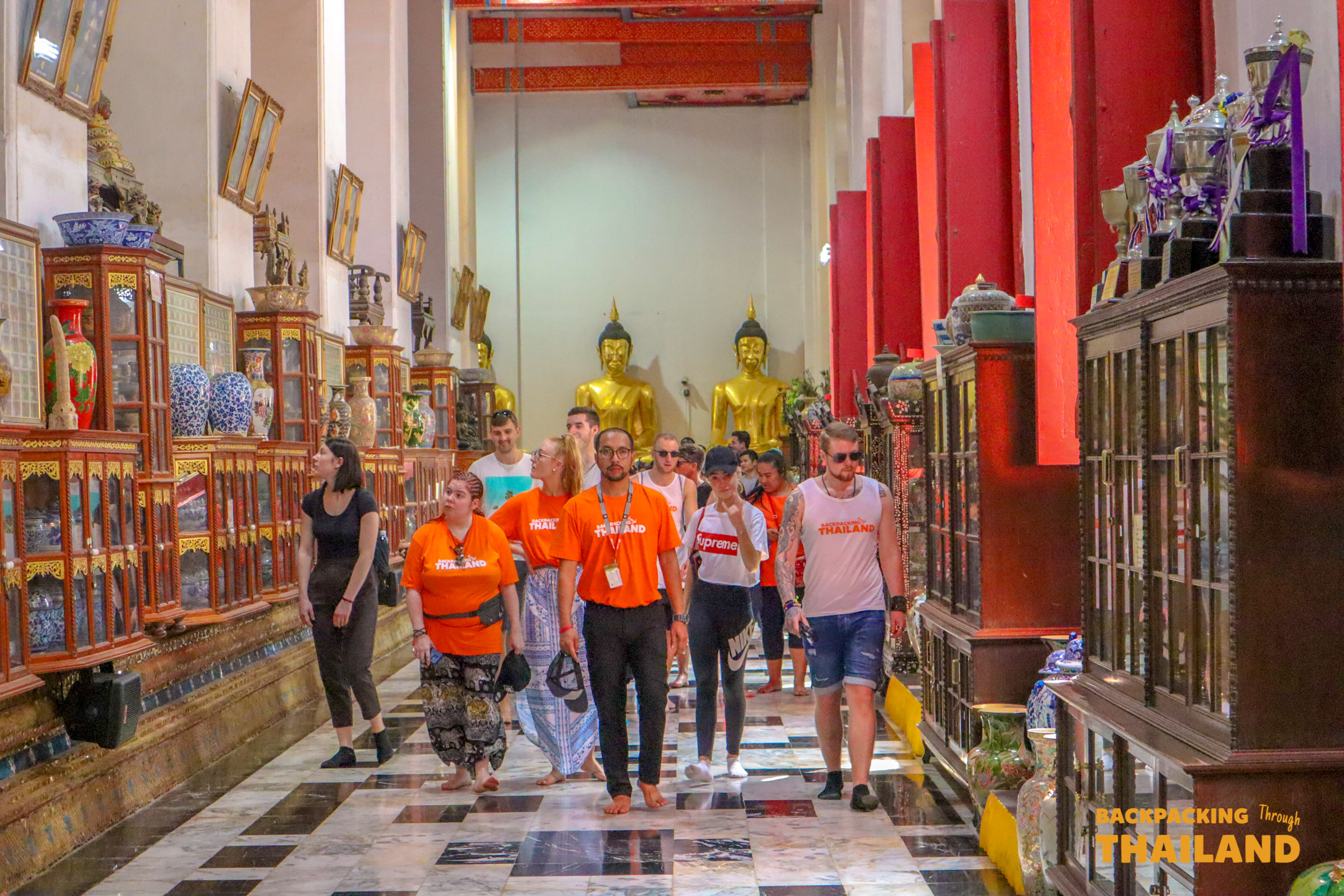 Tourists exploring a richly decorated Thai temple in Singburi with golden Buddha statues.