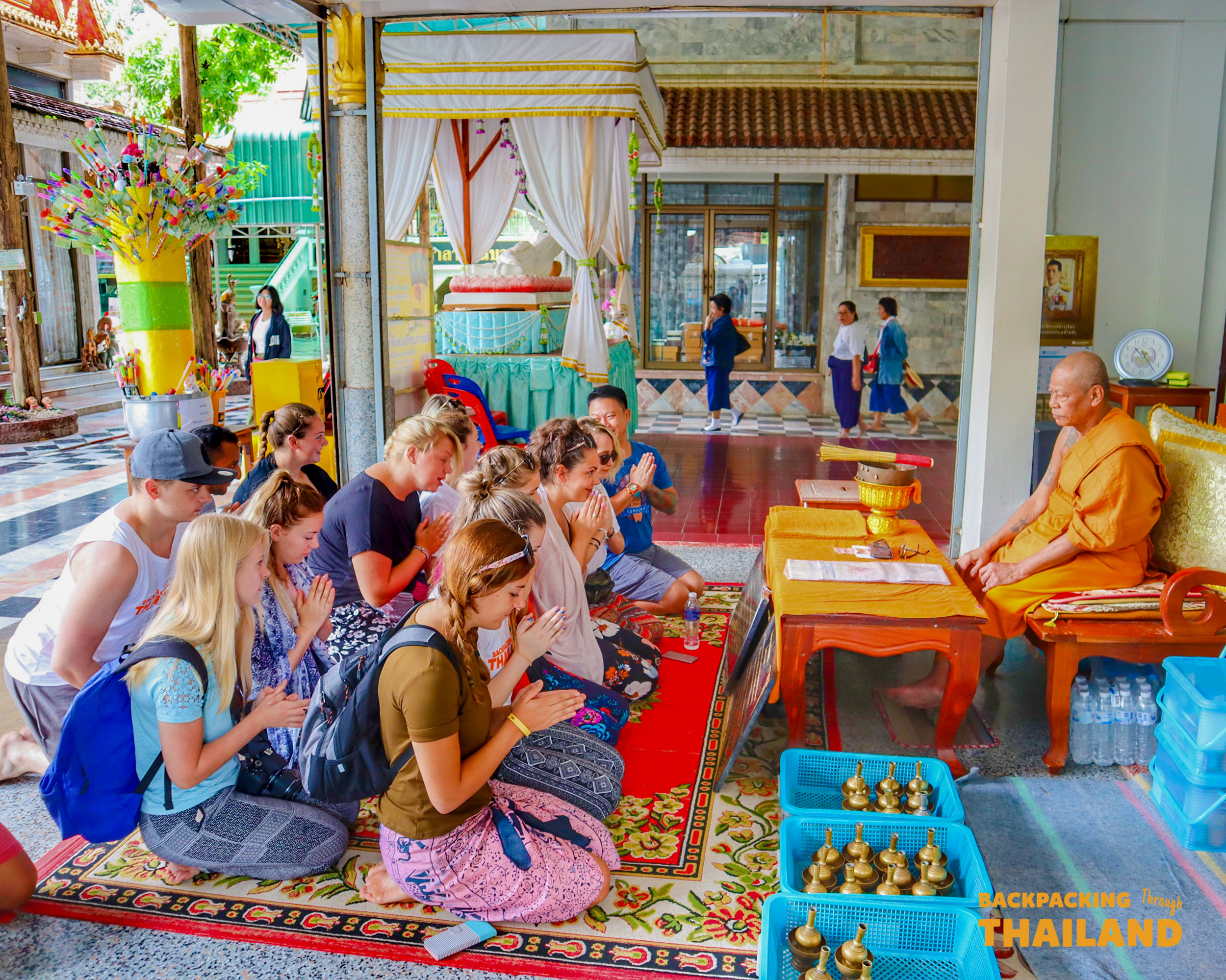 Backpackers receive a blessing from a Buddhist monk during a temple visit in Singburi, Thailand.