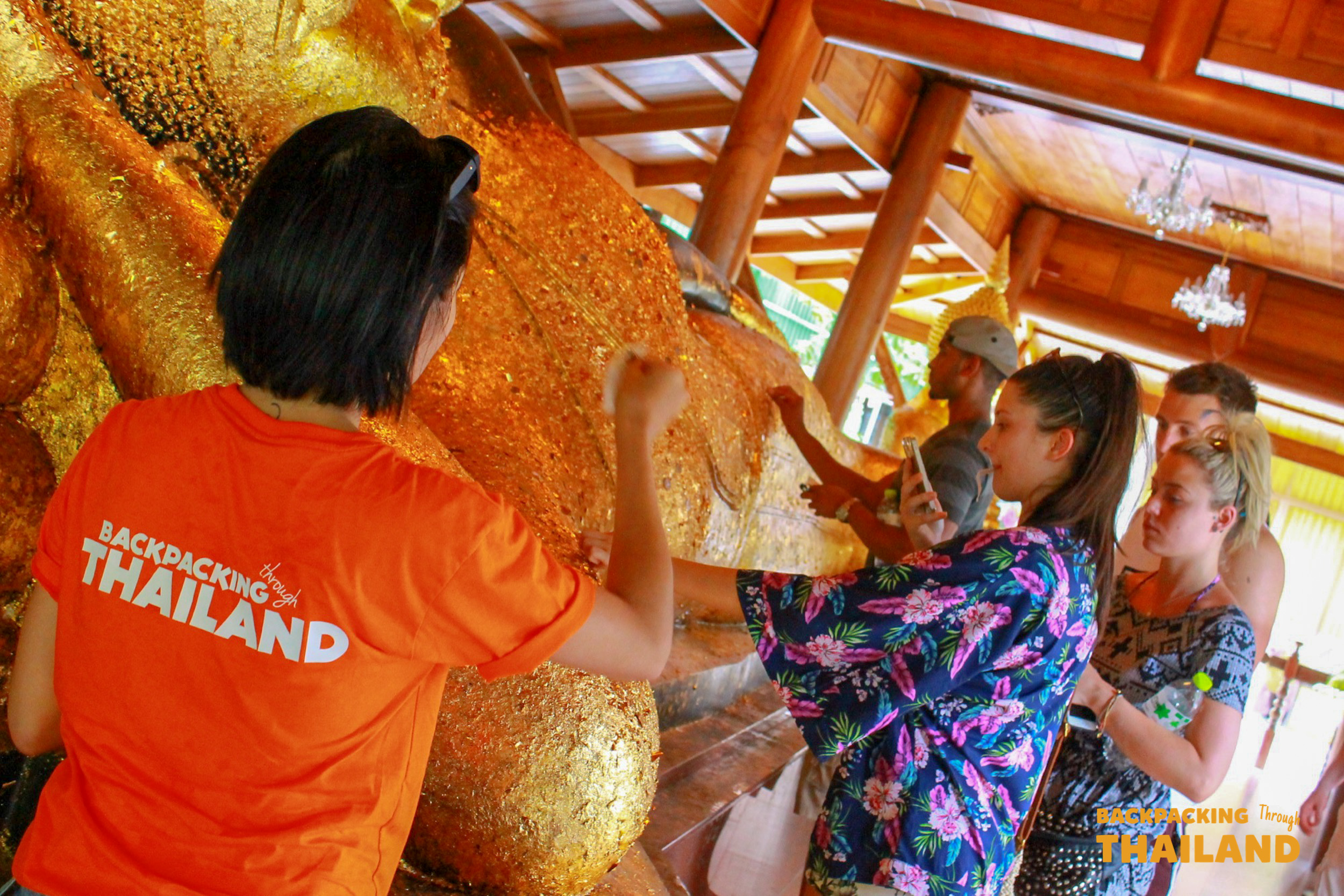 Backpackers reverently apply gold leaf to a large golden Buddha statue inside a temple in Singburi.