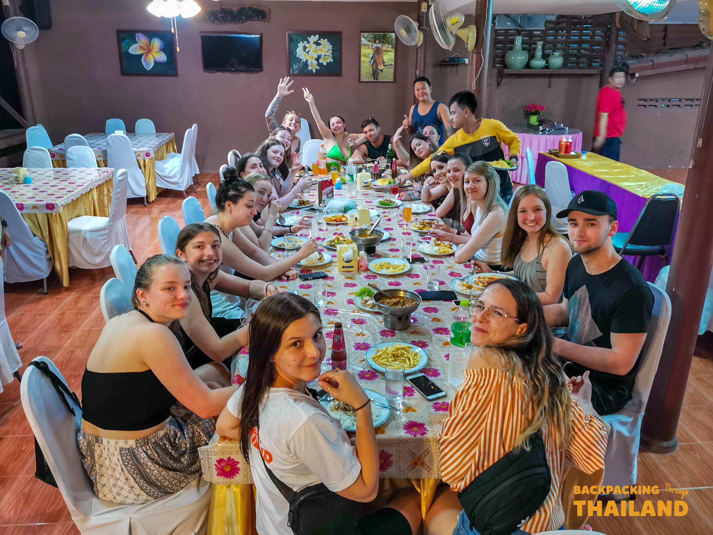 Happy backpackers share a lively group dinner at a resort restaurant in Singburi, Thailand.