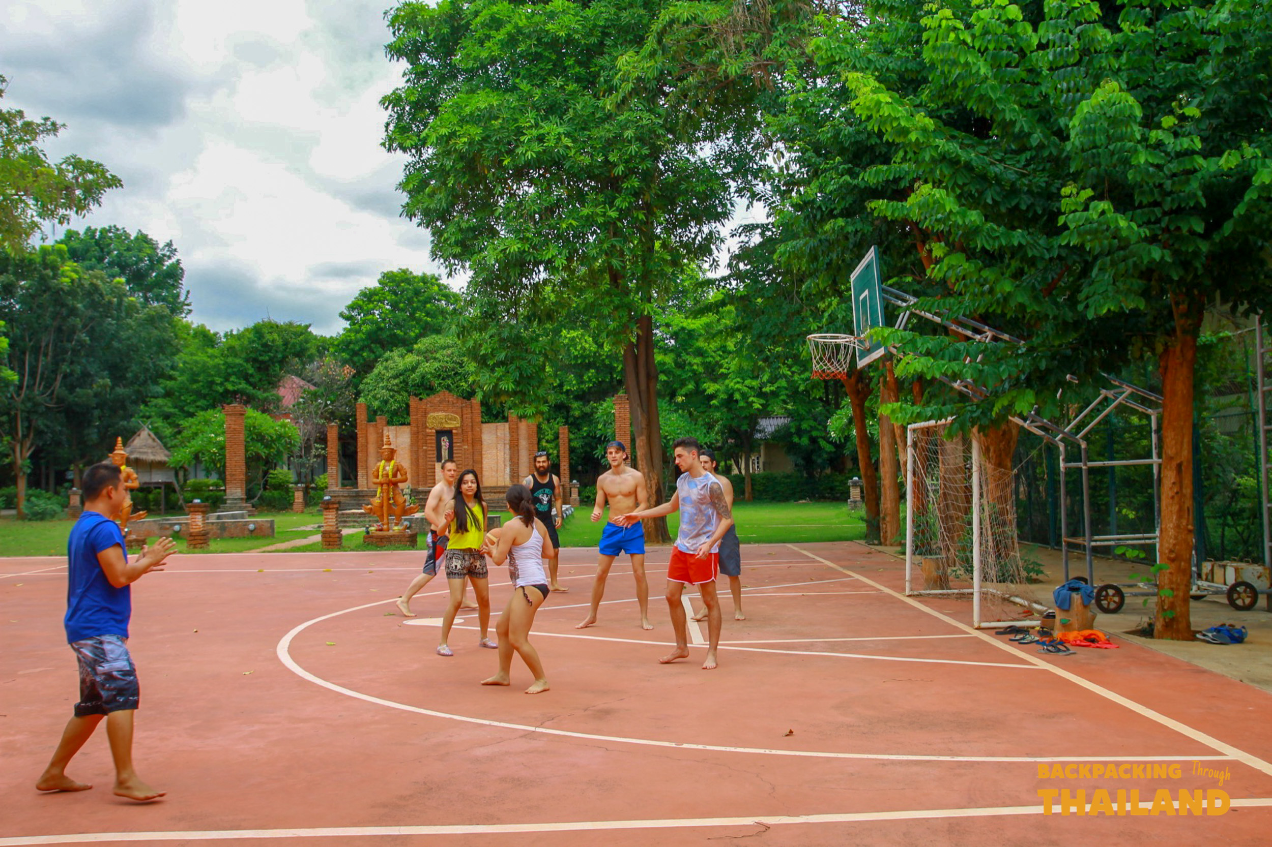 Backpackers enjoy a game of basketball on an outdoor court at a resort in Singburi, Thailand.