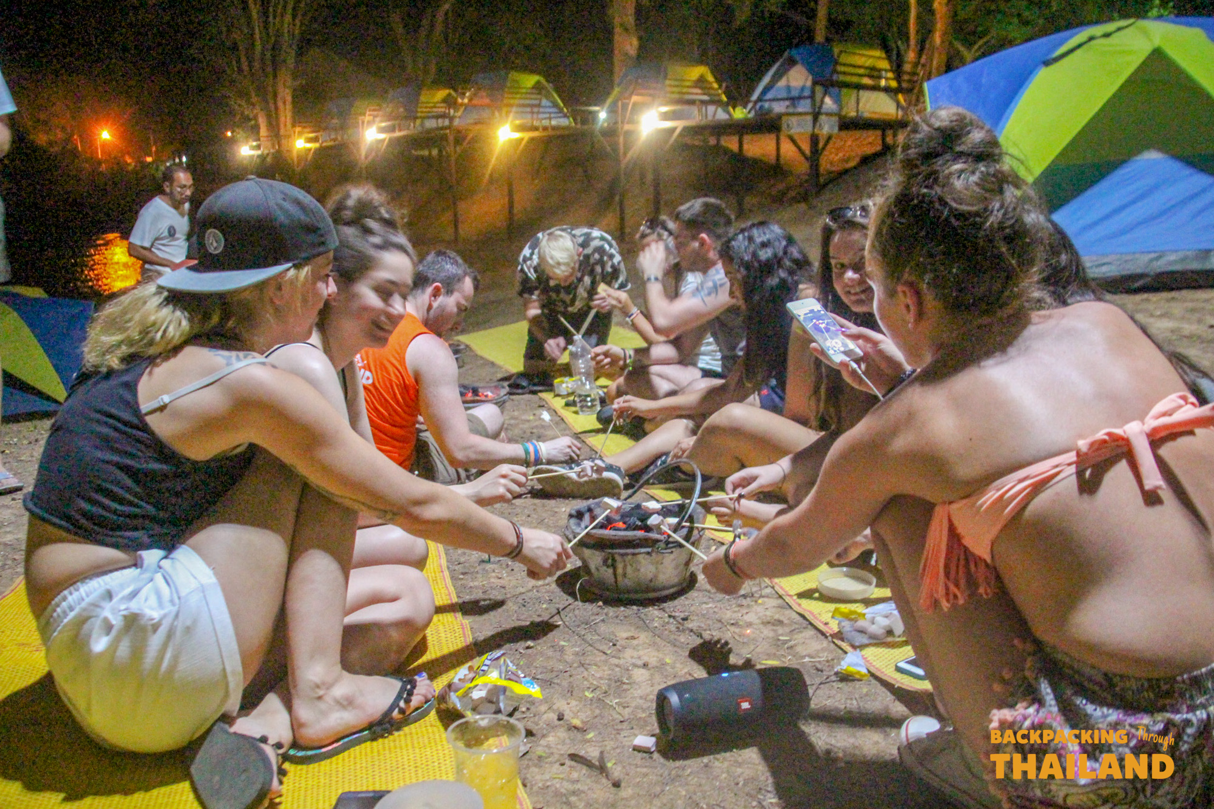 Backpacking group preparing food together on a large mat under hanging lights