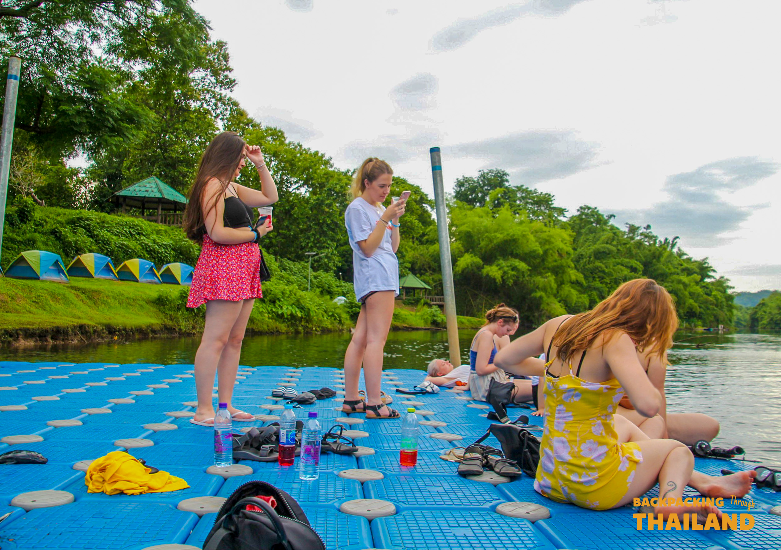 Backpacking group relaxing on a floating pontoon with food and drinks near a river