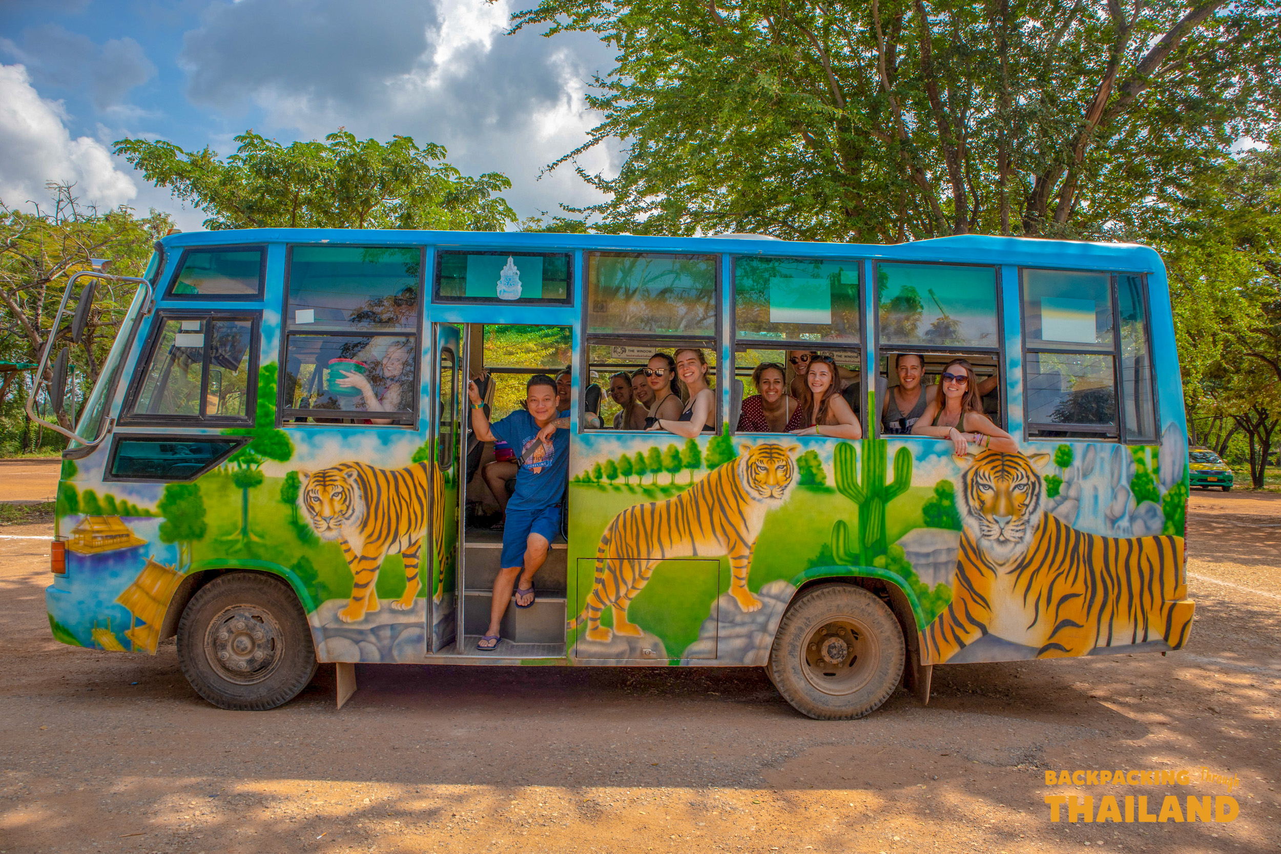 Happy backpackers enjoy a ride on a colorful tiger-painted bus at Erawan National Park in Thailand.