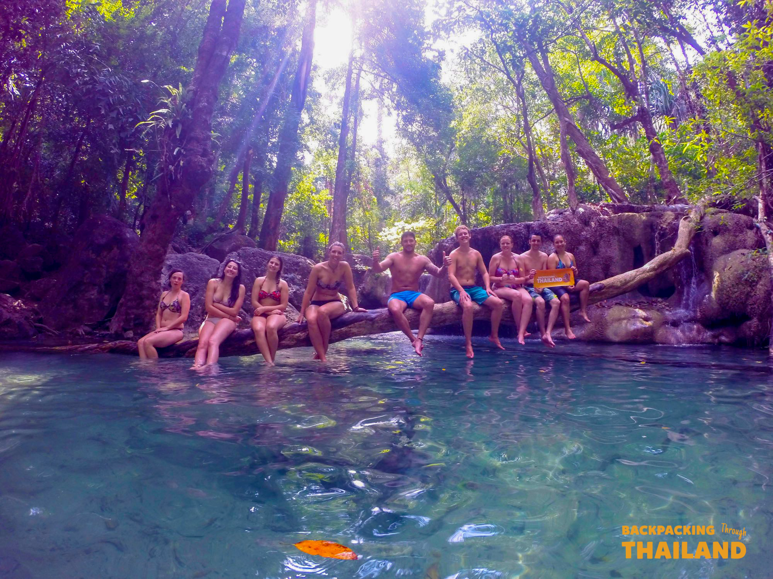 Backpacking group relaxing in an emerald natural pool surrounded by lush trees at Erawan National Park