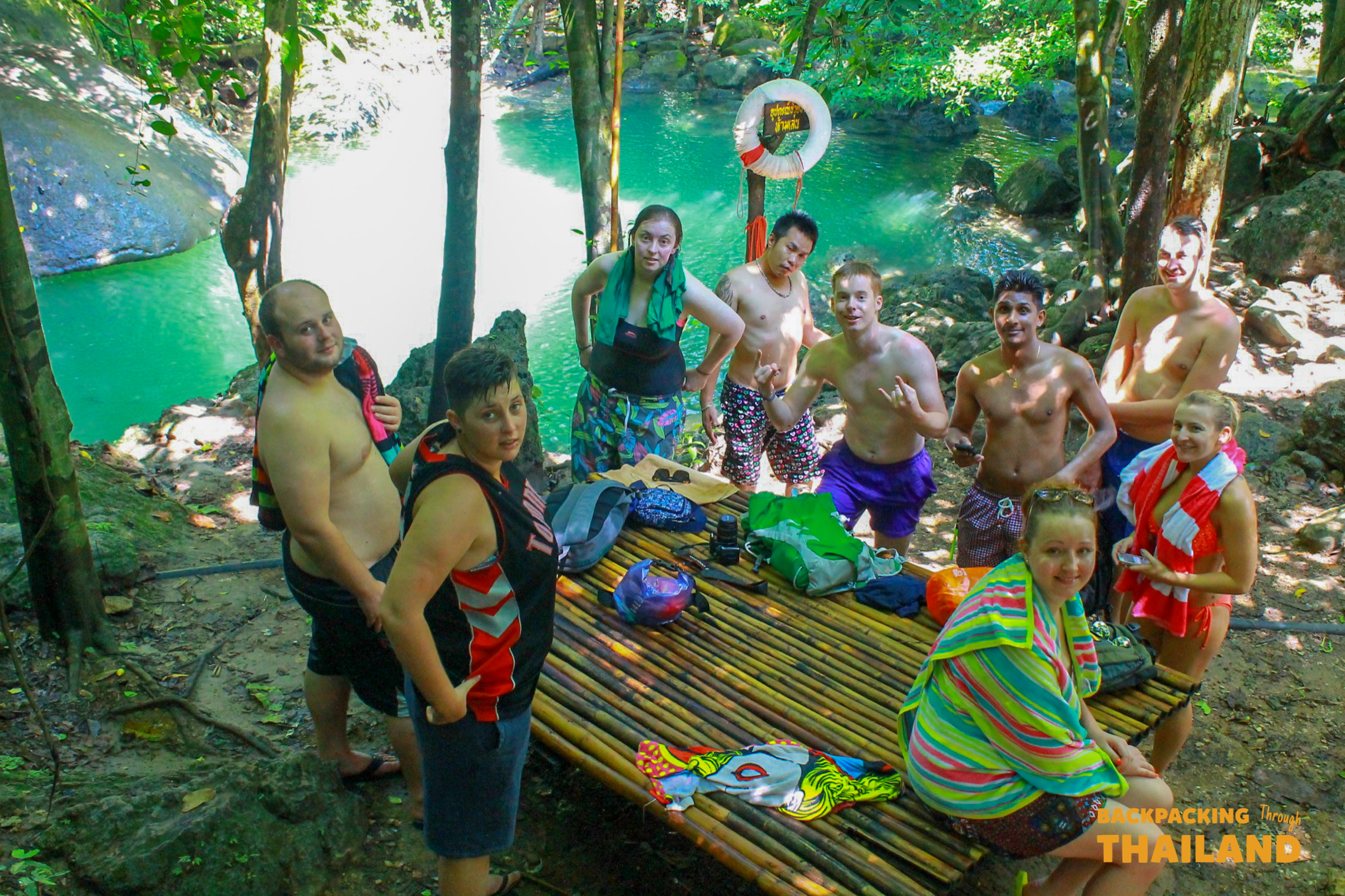 Backpacking group paddling a long-tail boat on a turquoise river in Erawan National Park