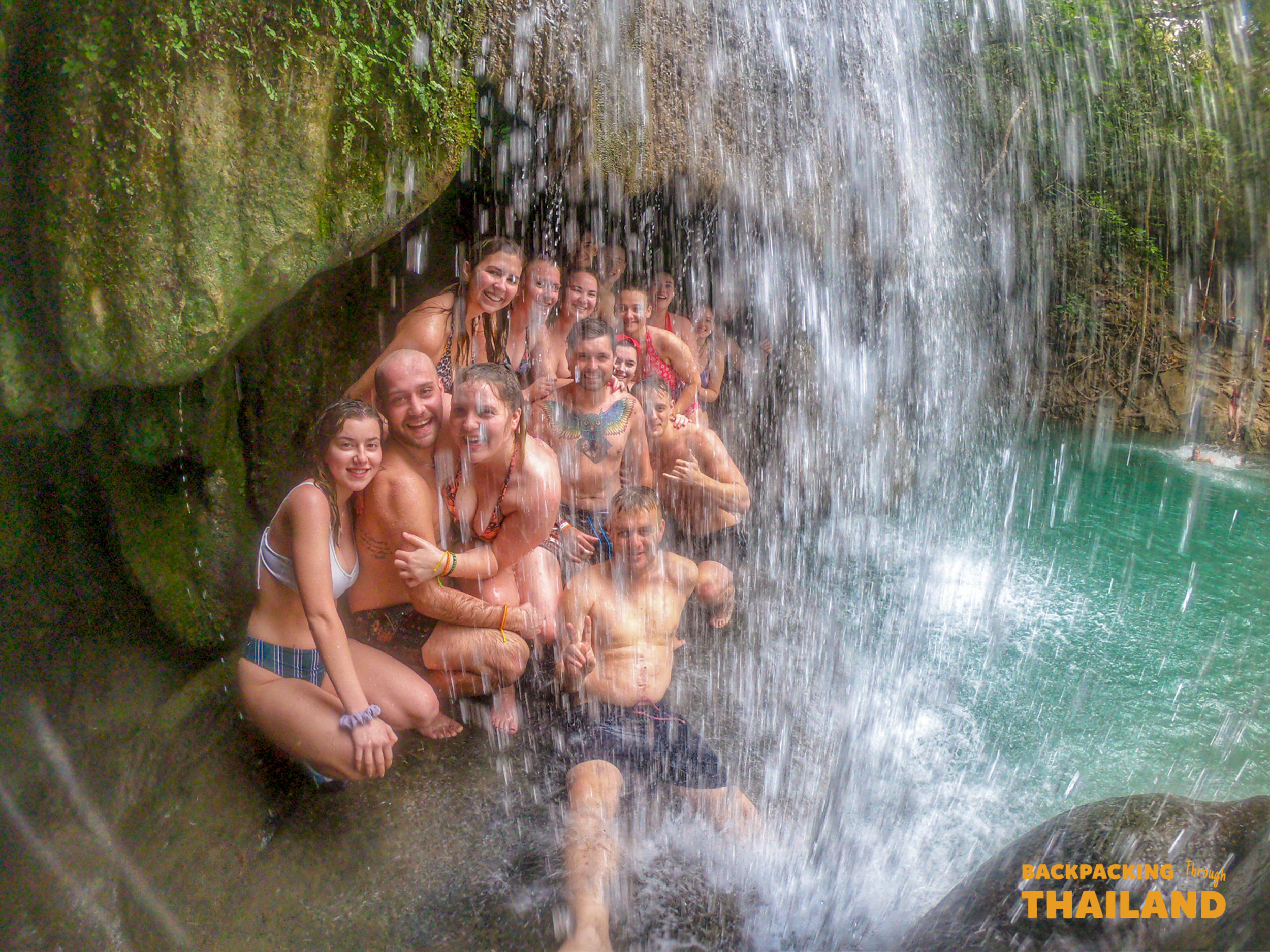 Backpacking group relaxing under a natural waterfall at Erawan National Park