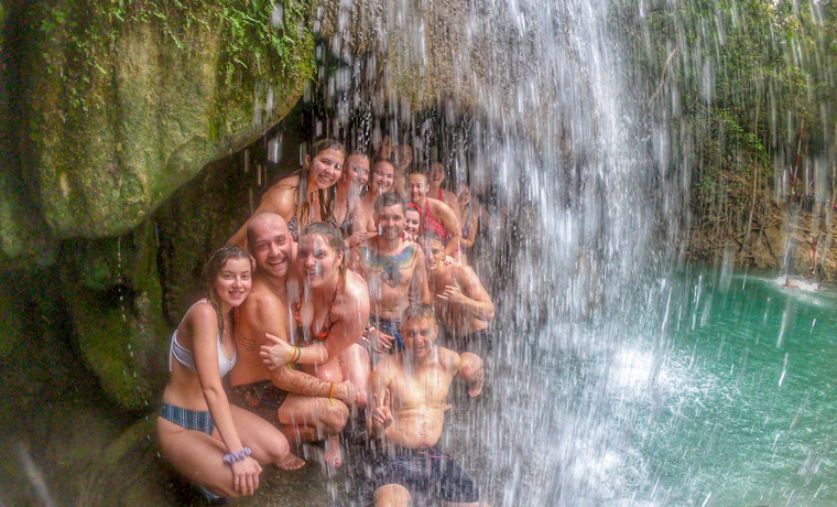 Smiling travelers cool off under the cascading waters of Erawan National Park in Thailand.