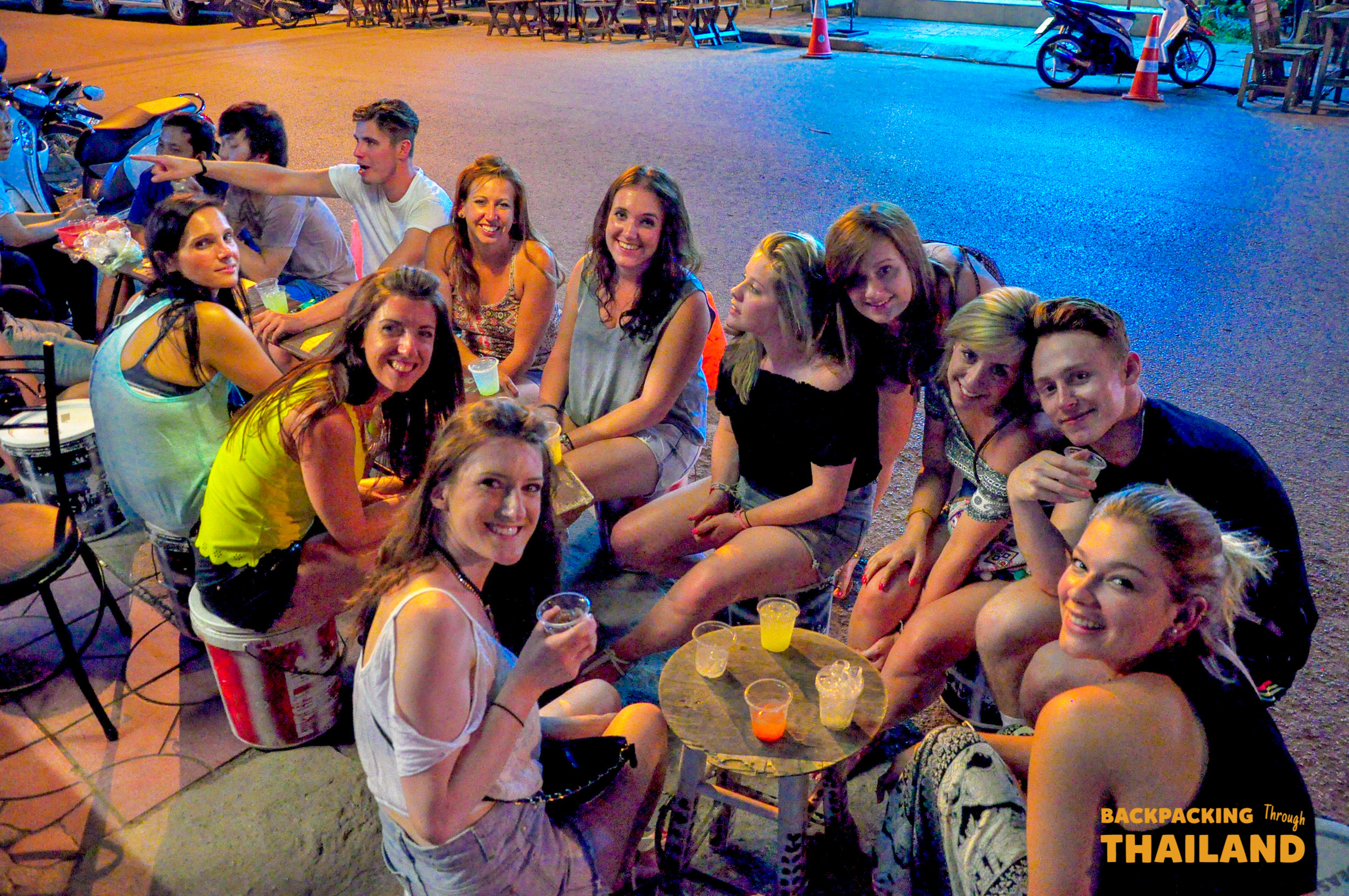 Backpacking group raising their drinks and smiling at a lively bar after a day at the elephant sanctuaryBackpacking group sitting around an elephant in a forest clearing during feeding time at the sanctuaryBackpacking group sitting with an elephant in a forest clearing during feeding time at the sanctuaryBackpacking group sitting with an elephant in a forest clearing during feeding time at the sanctuary