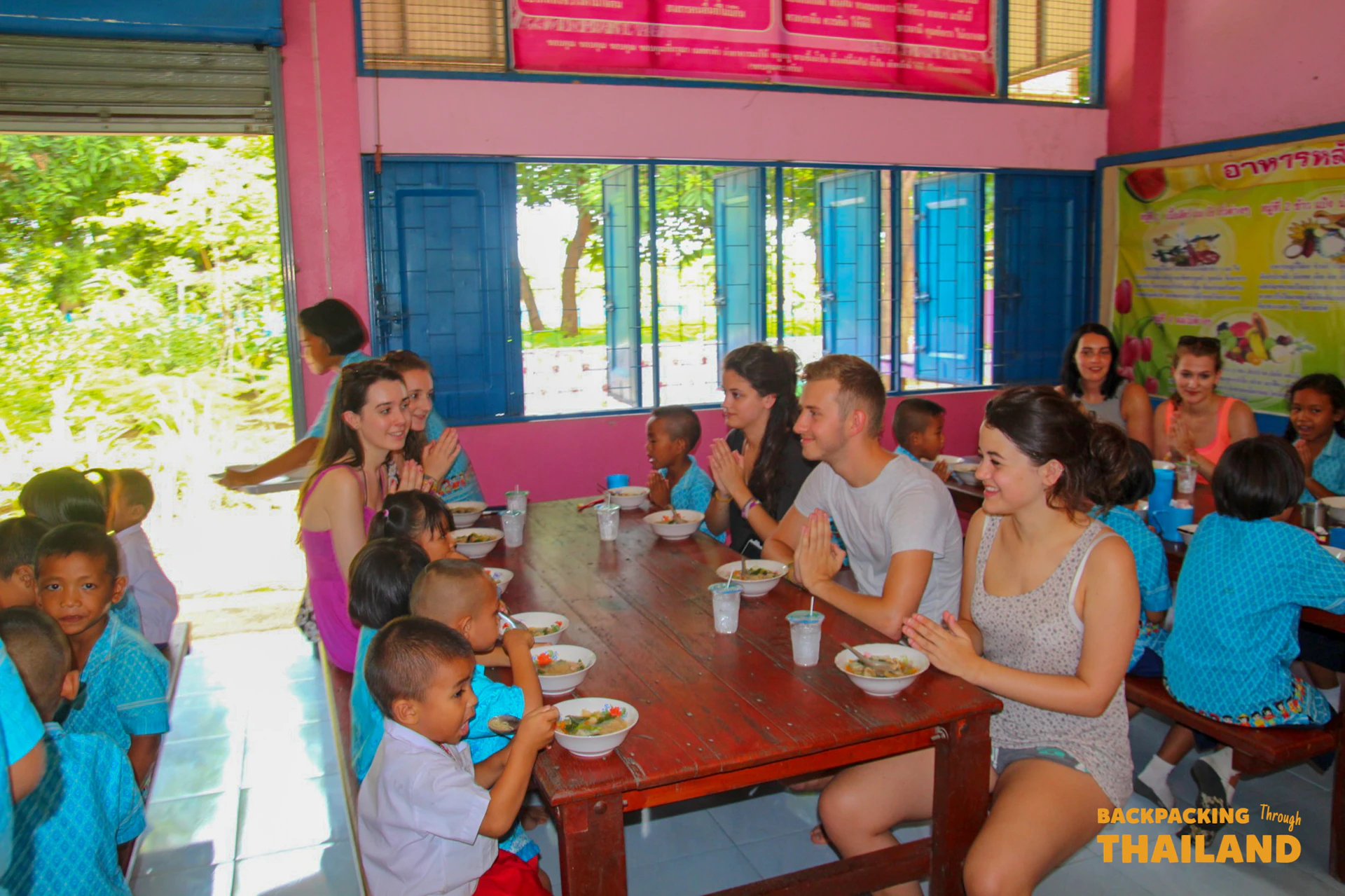 Backpackers and Thai children share a communal meal at a school in Thailand.
