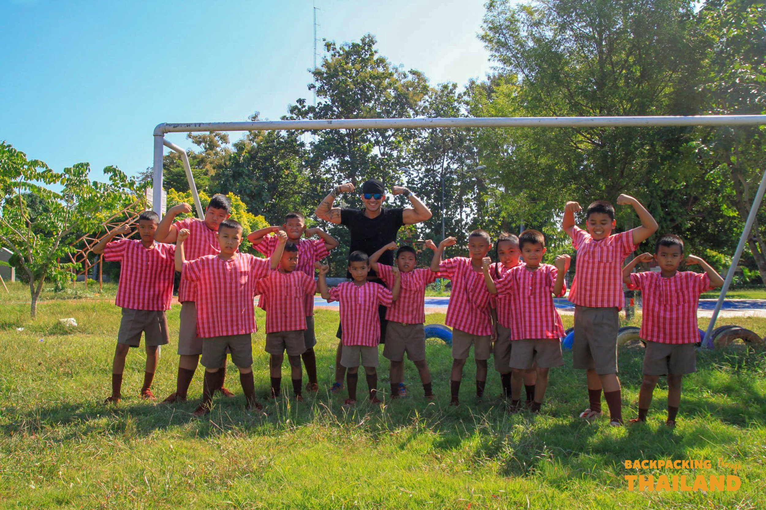 Backpacking group and Thai schoolchildren posing together on a grassy field at a rural school