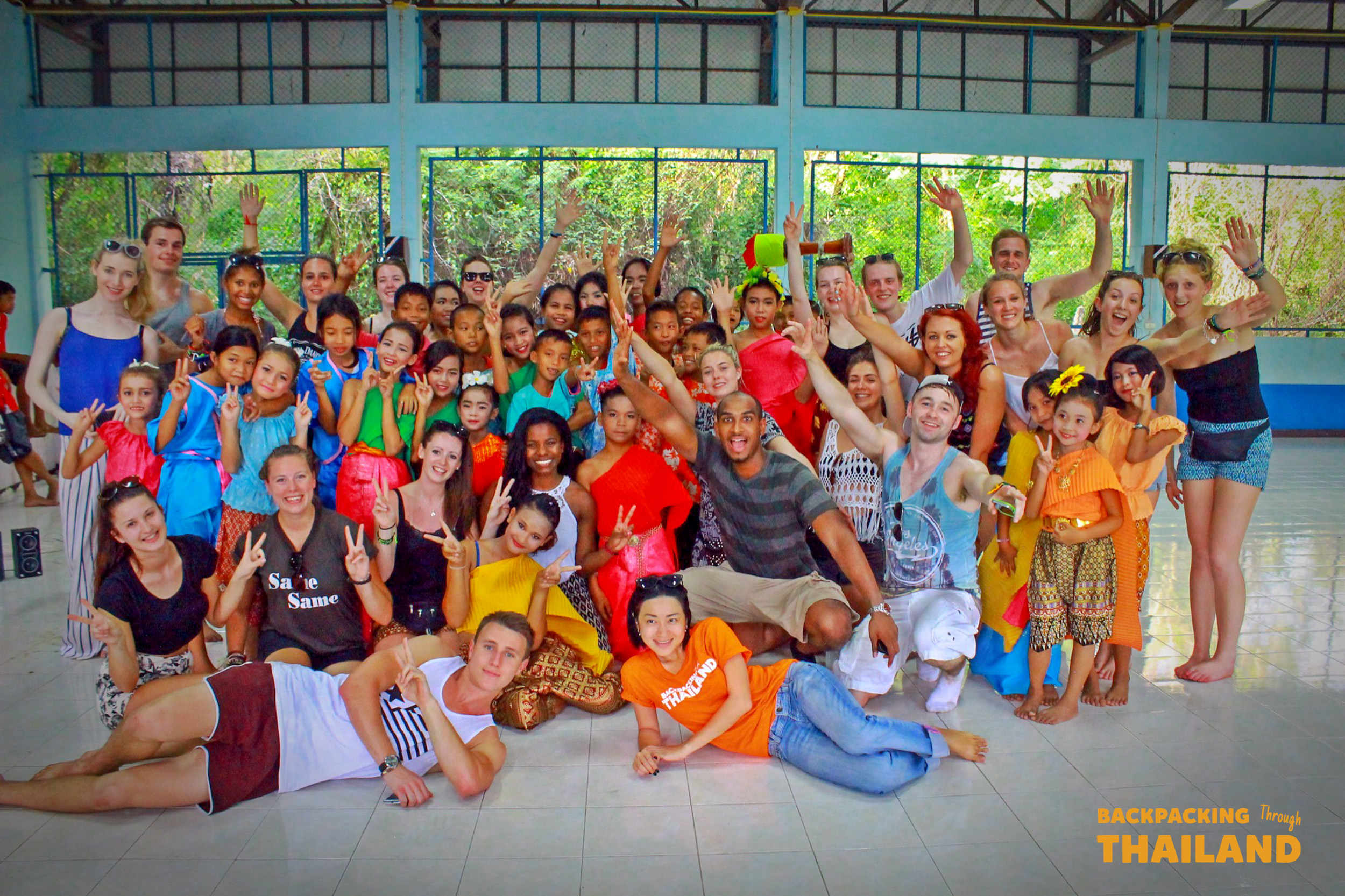 Happy backpackers and local students pose for a group photo during a school visit in Thailand.