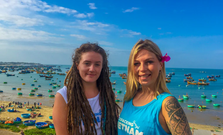 Two happy women overlook Mui Ne fishing village with numerous colorful boats on the beach.