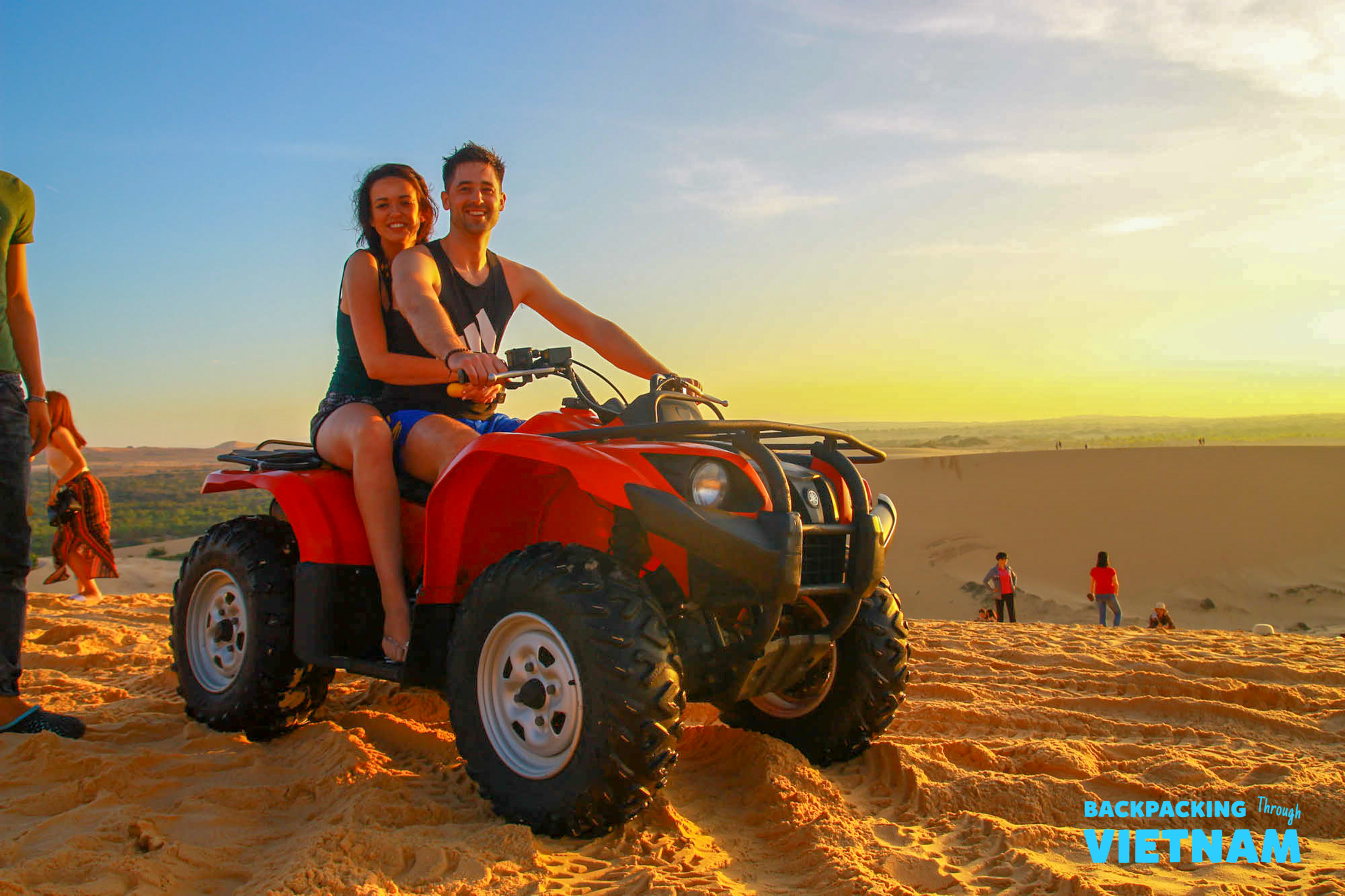 Friends riding quad bike on red dunes at sunrise