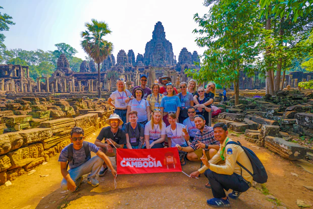 A group of happy backpackers pose with a banner in front of the ancient Bayon temple, Cambodia.