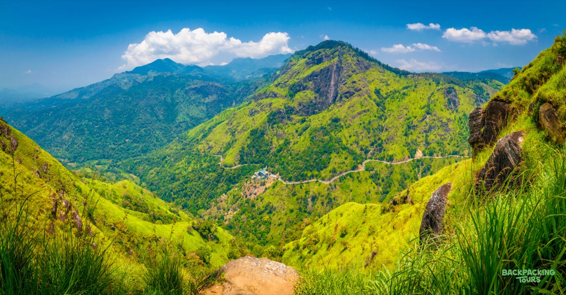 Lush green mountains and valleys under a bright blue sky with a winding road in Sri Lanka.
