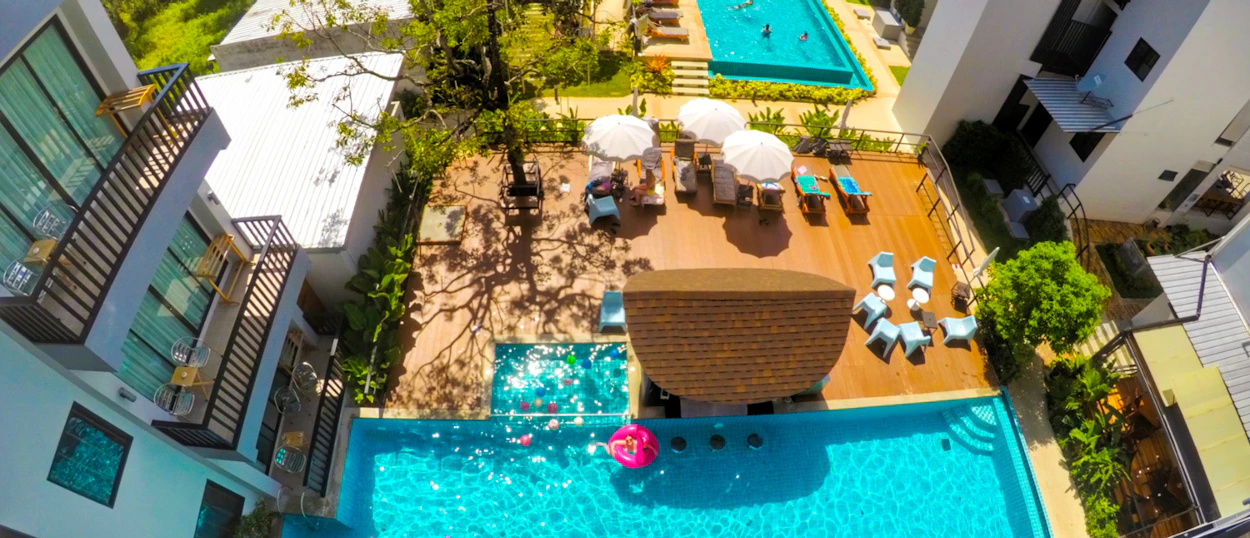 Aerial view of a hotel pool area in Krabi with guests swimming and relaxing under umbrellas.