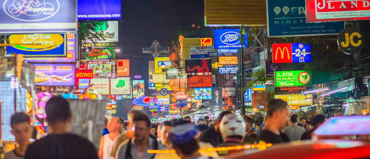 A bustling night scene on Khao San Road, with crowds of people and many colorful neon signs.