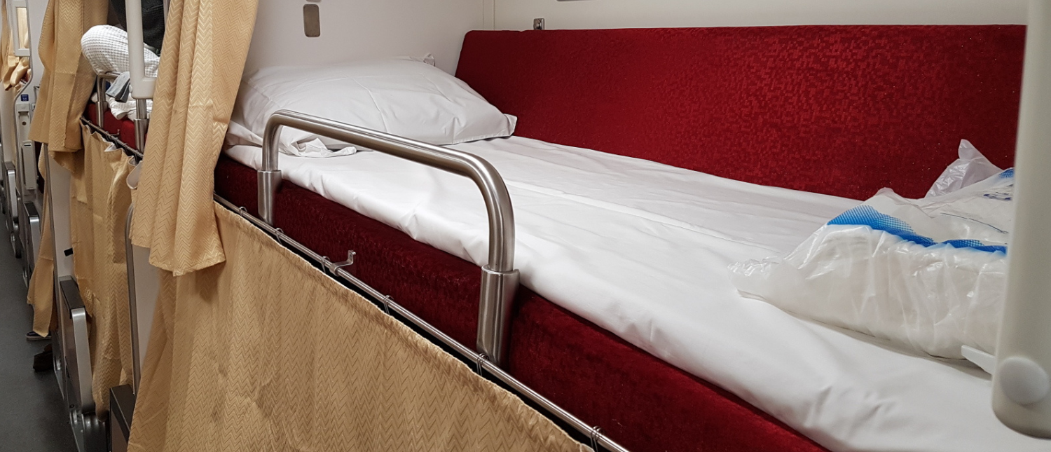 Overnight train sleeper berth with red bedding on a Thai train
