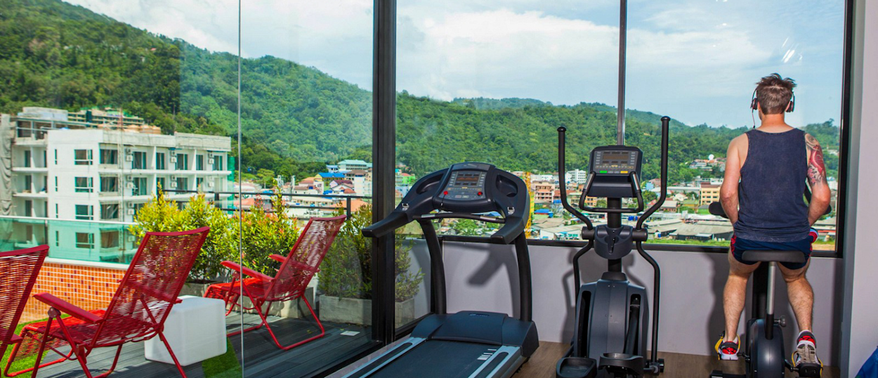 Traveller using treadmills at rooftop gym with scenic view at The Crib hotel in Phuket