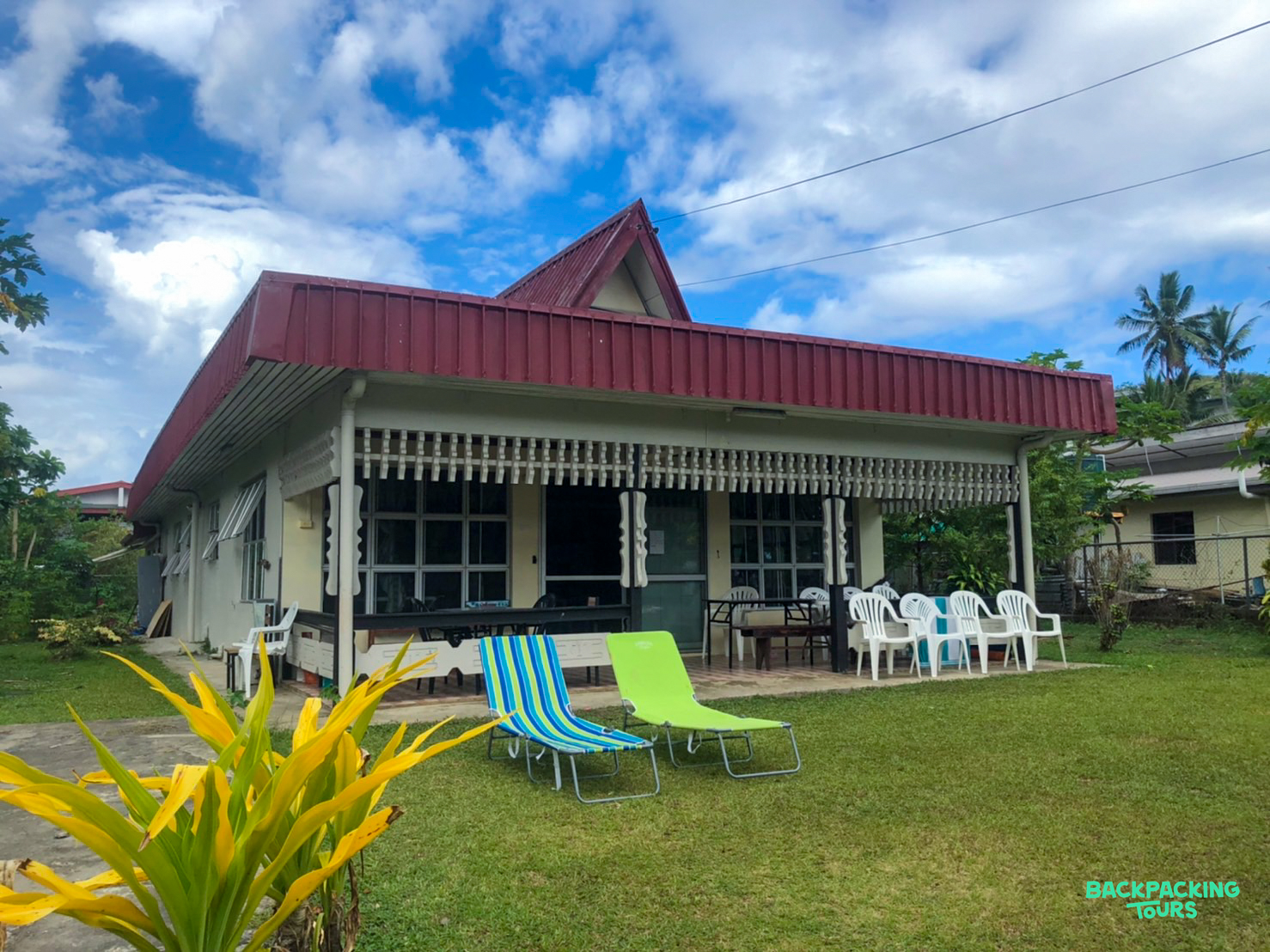 A red-roofed house with a green lawn and lounge chairs, offering comfortable accommodation in Fiji.