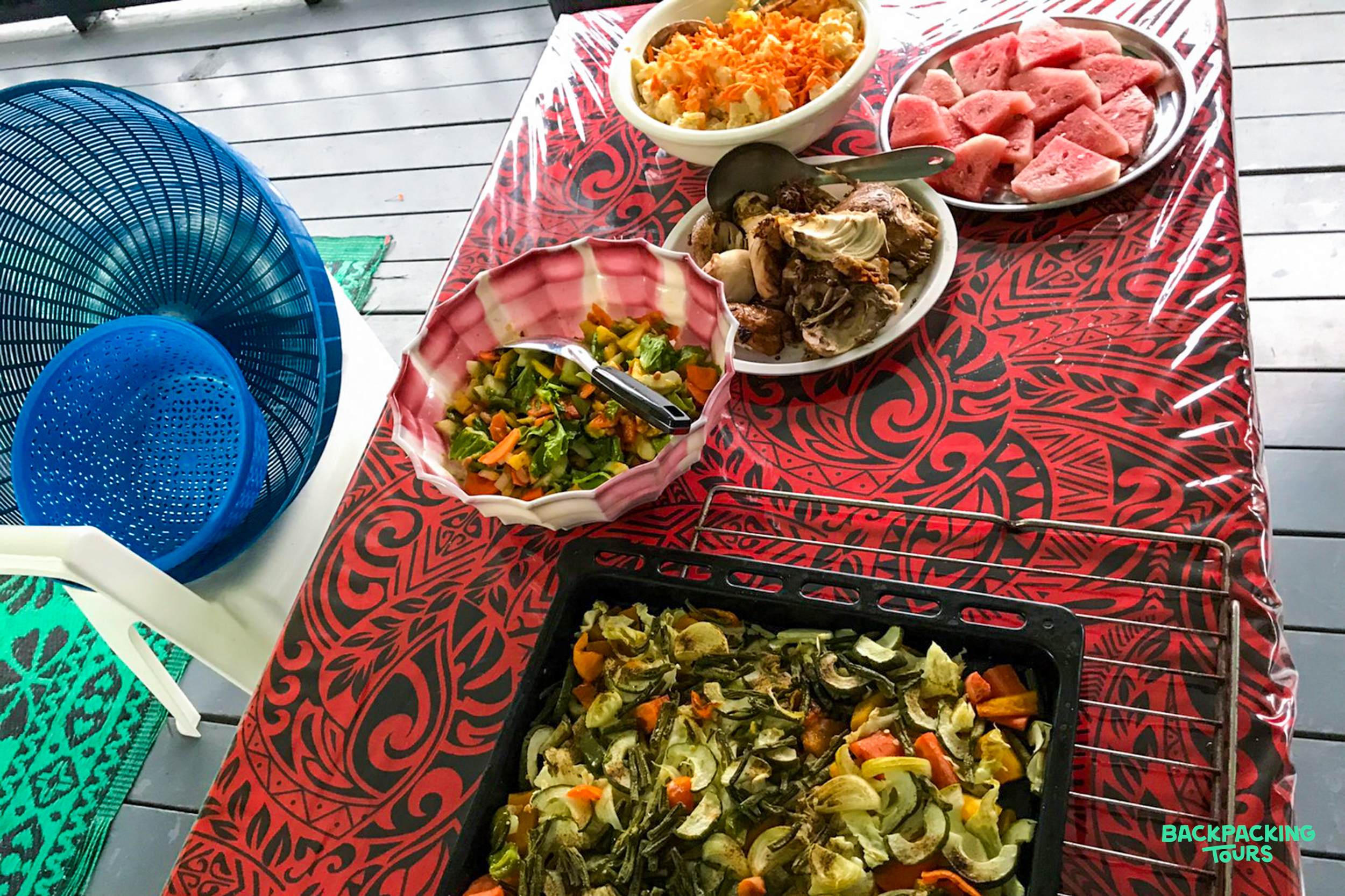 A colorful buffet of roasted vegetables, fresh watermelon, fruit salad, and other dishes on a patterned table.
