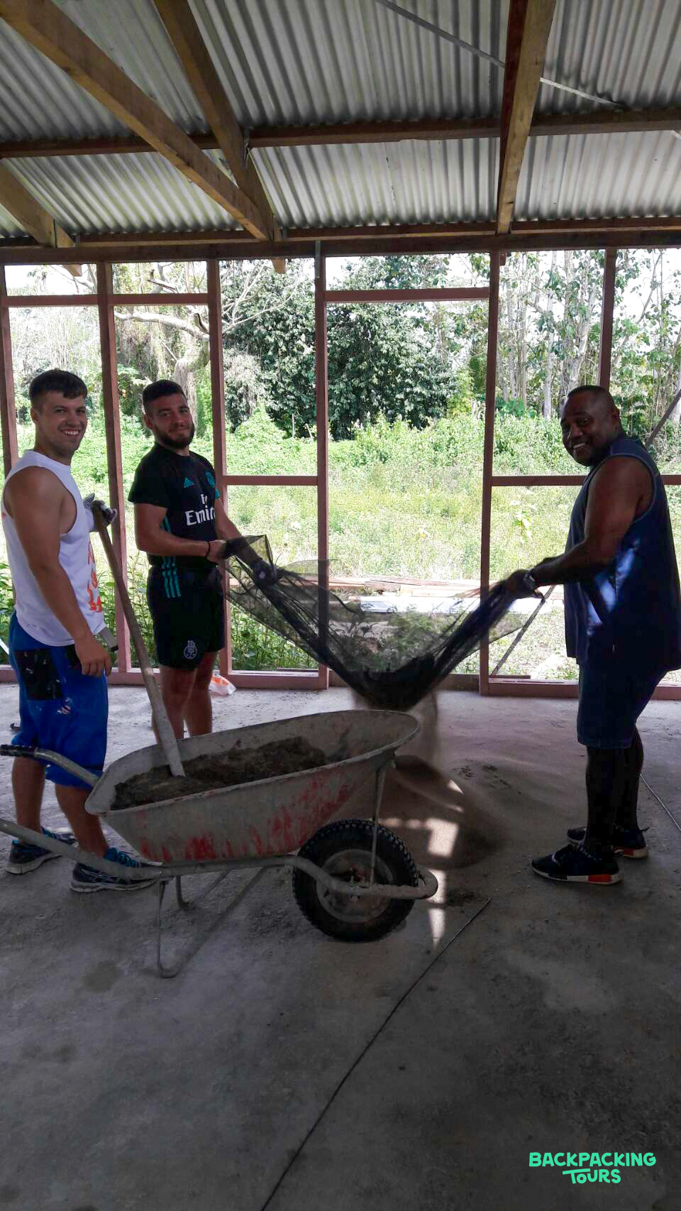 Three men smiling while sifting building materials at a construction site in Fiji.