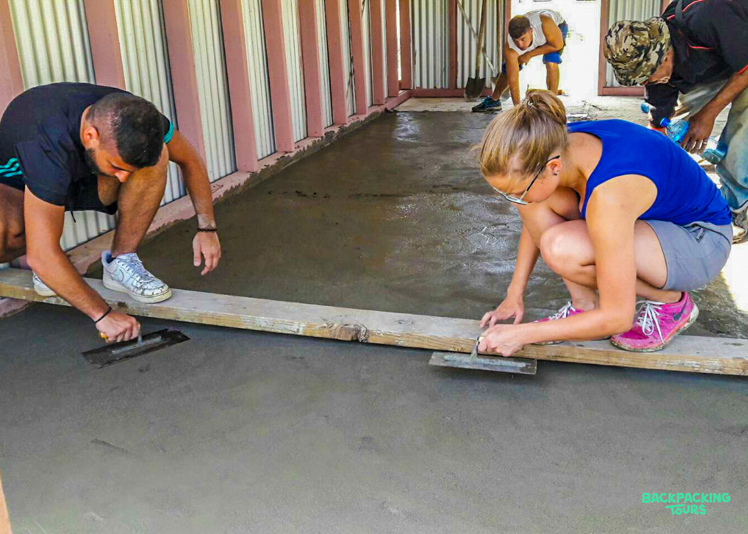 A group of volunteers carefully smooth a newly poured concrete floor during a renovation.