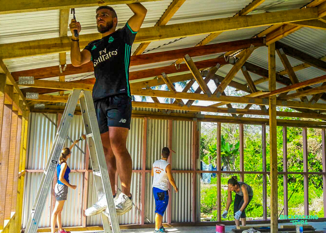 Volunteers work together to renovate a building, installing ceiling elements and painting walls.