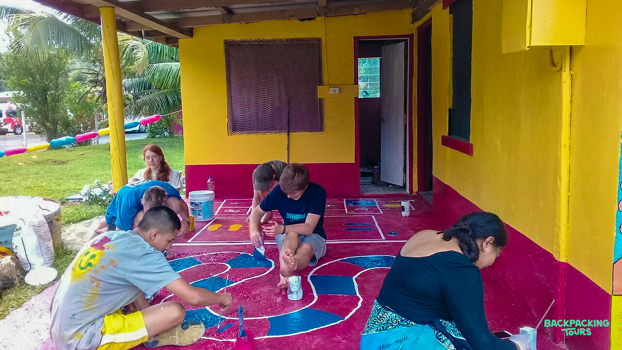 Volunteers paint a vibrant, colorful mural on the floor of a kindergarten porch.