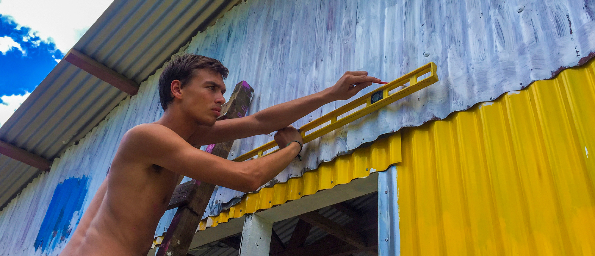 Volunteer on a ladder carefully levels a corrugated metal wall during a renovation project.