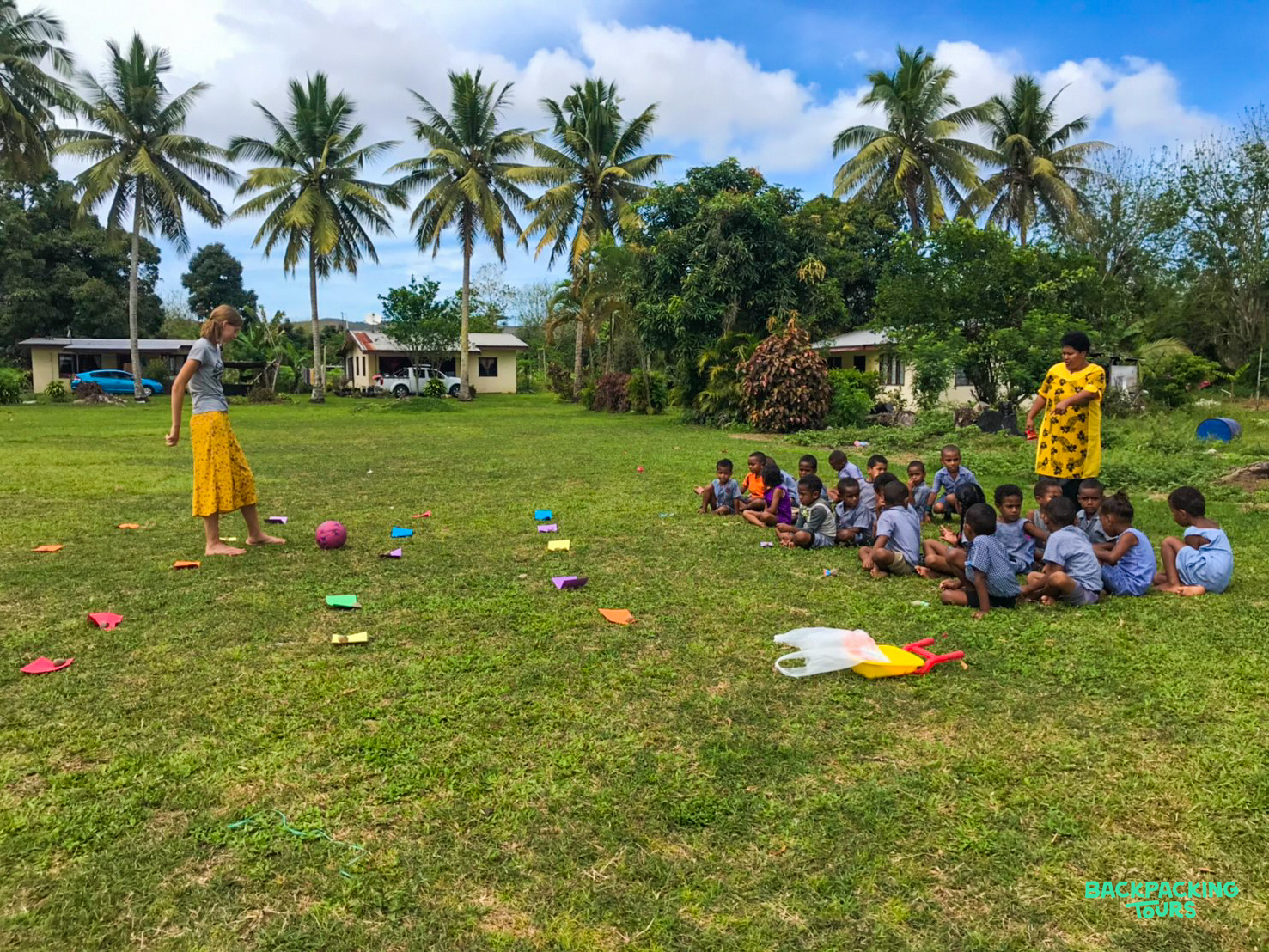 A volunteer plays an outdoor game with kindergarten children under palm trees in Fiji.