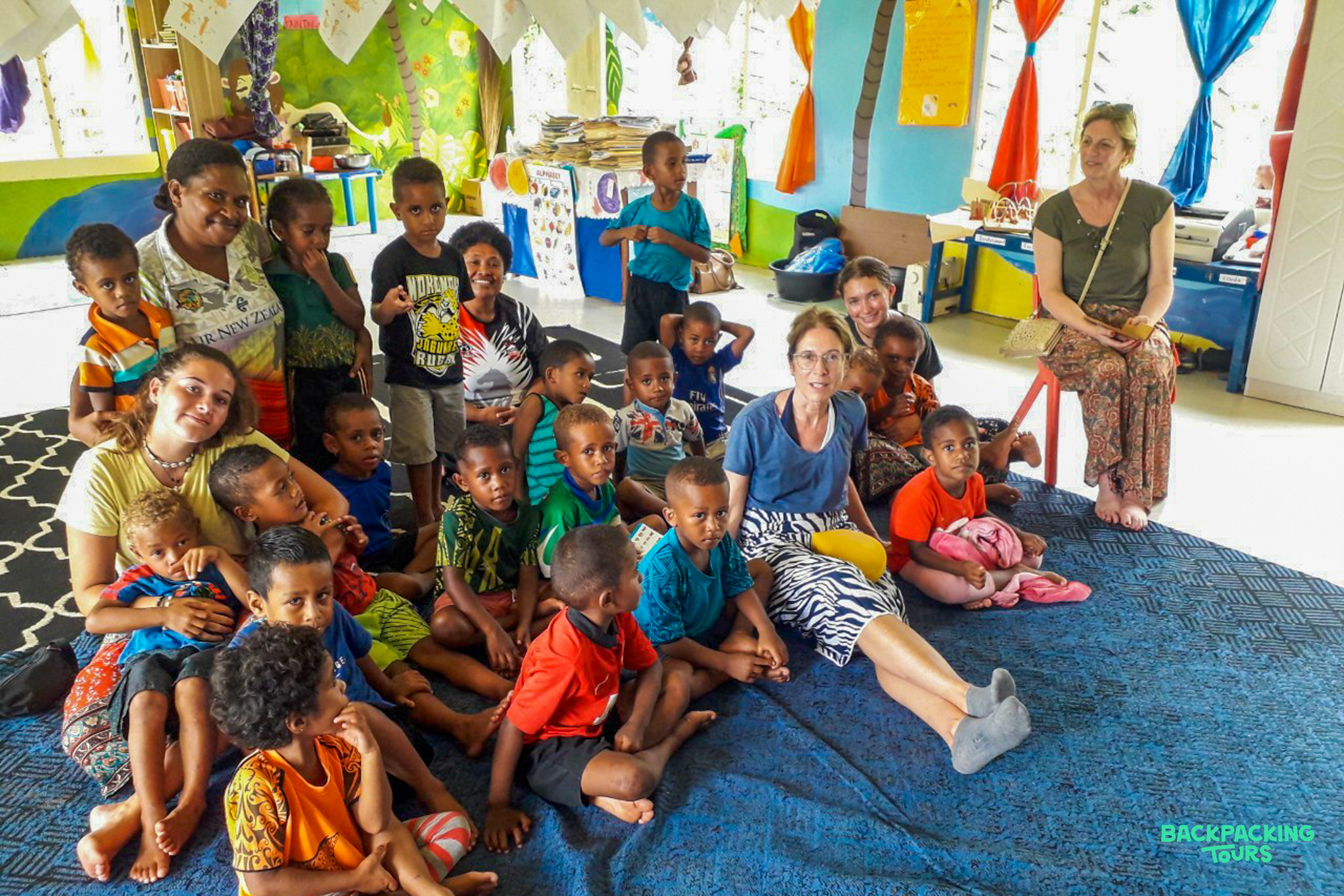 Happy children and women volunteers pose together in a brightly decorated kindergarten classroom in Fiji.