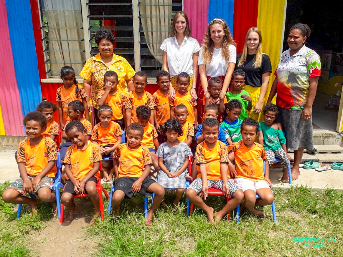 Smiling children and volunteers pose together outside a brightly painted kindergarten in Fiji.